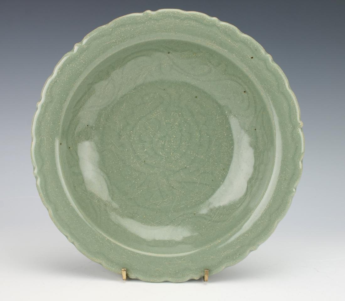 MING DYNASTY INCISED CELADON BOWL: MING DYNASTY INCISED CELADON BOWL: A celadon bowl that has a scalloped pie crust rim with incised lotus in the center surrounded by a wide tendril border. The bottom repeats the wide tendril border. T