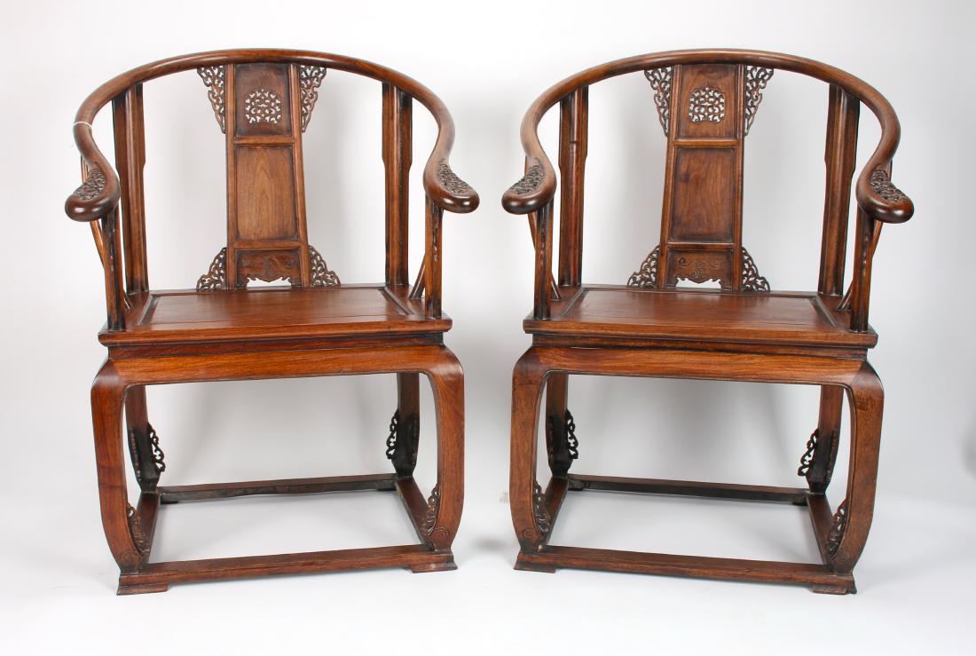 PAIR OF HUANGHUALI HORSESHOE CHAIRS: PAIR OF HUANGHUALI HORSESHOE CHAIRS: Two pierced and carved horseshoe back chairs with pierced and carved flanges on the top and bottom. The bottom has an incised panel. The hand rest on the arms are 