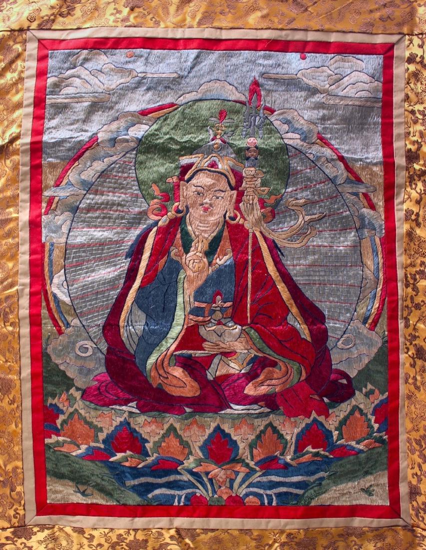 RARE EMBROIDERED SILK THANGKA OF BUDDHA: RARE EMBROIDERED SILK THANGKA OF BUDDHA: Embroidered thangka of Buddha matted in silk dragon patterned brocade. The Buddha is holding a censer and a vajra, and a decorative spear against his body. He 
