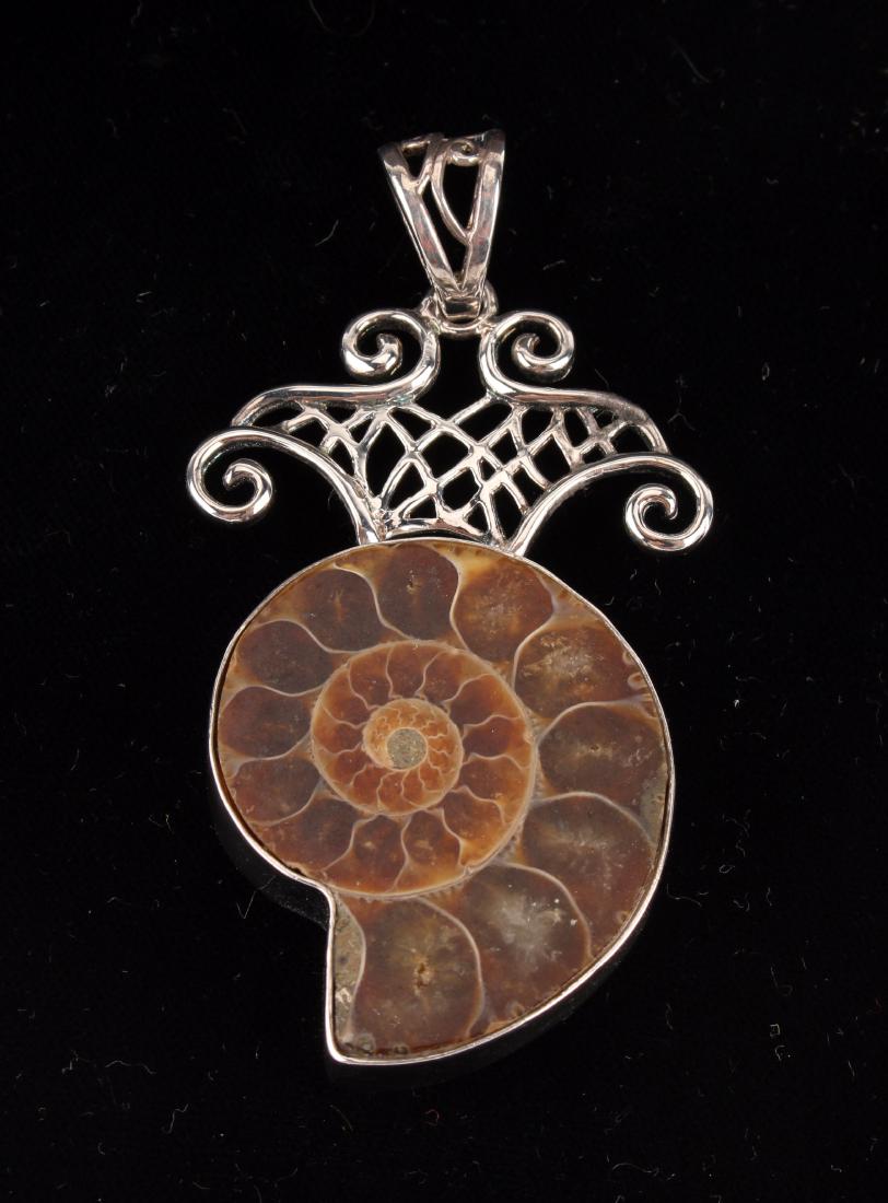 LARGE AMMONITE FOSSIL PENDANT: LARGE AMMONITE FOSSIL PENDANT: Bezel set in sterling and topped with an unusual curvilinear filigree design. Would look ideal on a chain or neck wire. The "V" shapes bale is marked on the ba