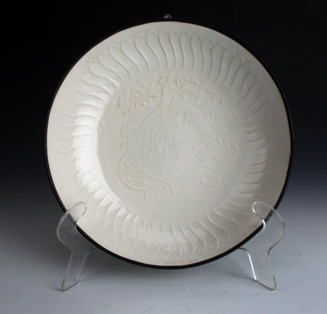 DING WARE BOWL: DING WARE BOWL: This bowl is on the smaller side, embossed with a wading bird among foliage and a scholar's stone. The border has overlapping petals under an unglazed rim. Sits on a very low foot.