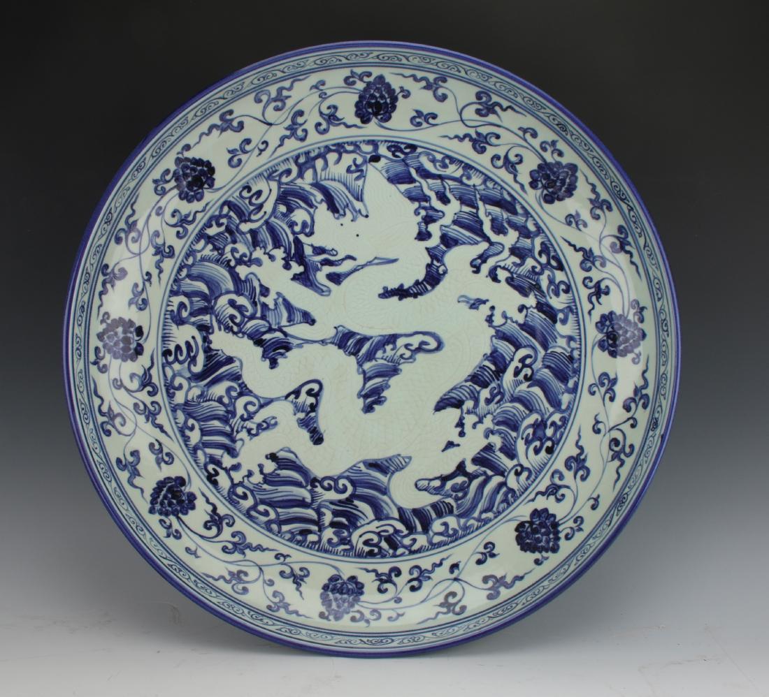 LARGE BLUE AND WHITE REVERSE DRAGON MING CHARGER: LARGE BLUE AND WHITE REVERSE DRAGON MING CHARGER: The central image is a reverse dragon with incised scales that are defined by the pooling of glaze. His outstretched claws swirl among wave patterns.