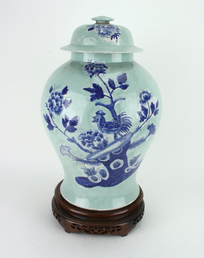 LARGE GINGER JAR WITH ROOSTER ON STAND: LARGE GINGER JAR WITH ROOSTER ON STAND: A rooster stands on a boulder among flowers on a light blue background. Lid has flowers on the front. Has pierced wooden stand. 10&quo