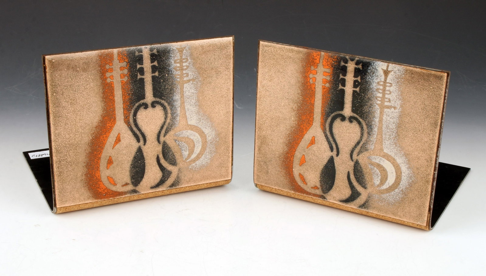 PAIR OF MCM COPPER ENAMELED MUSIC BOOKENDS: PAIR OF MCM COPPER ENAMELED MUSIC BOOKENDS: They have images of mandolin, banjo, and a guitar in white, black and orange on a coppery ground. Cork on the bottom. 5" X 4 1