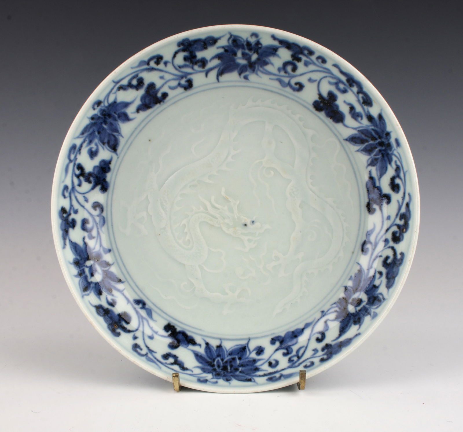 BLUE & CELADON PORCELAIN BOWL: BLUE & CELADON PORCELAIN BOWL: Raised bas relief dragon in the center in white on a celadon ground surrounded by a flower and tendril border in blue. Flower and tendril on the back. Has unglazed f