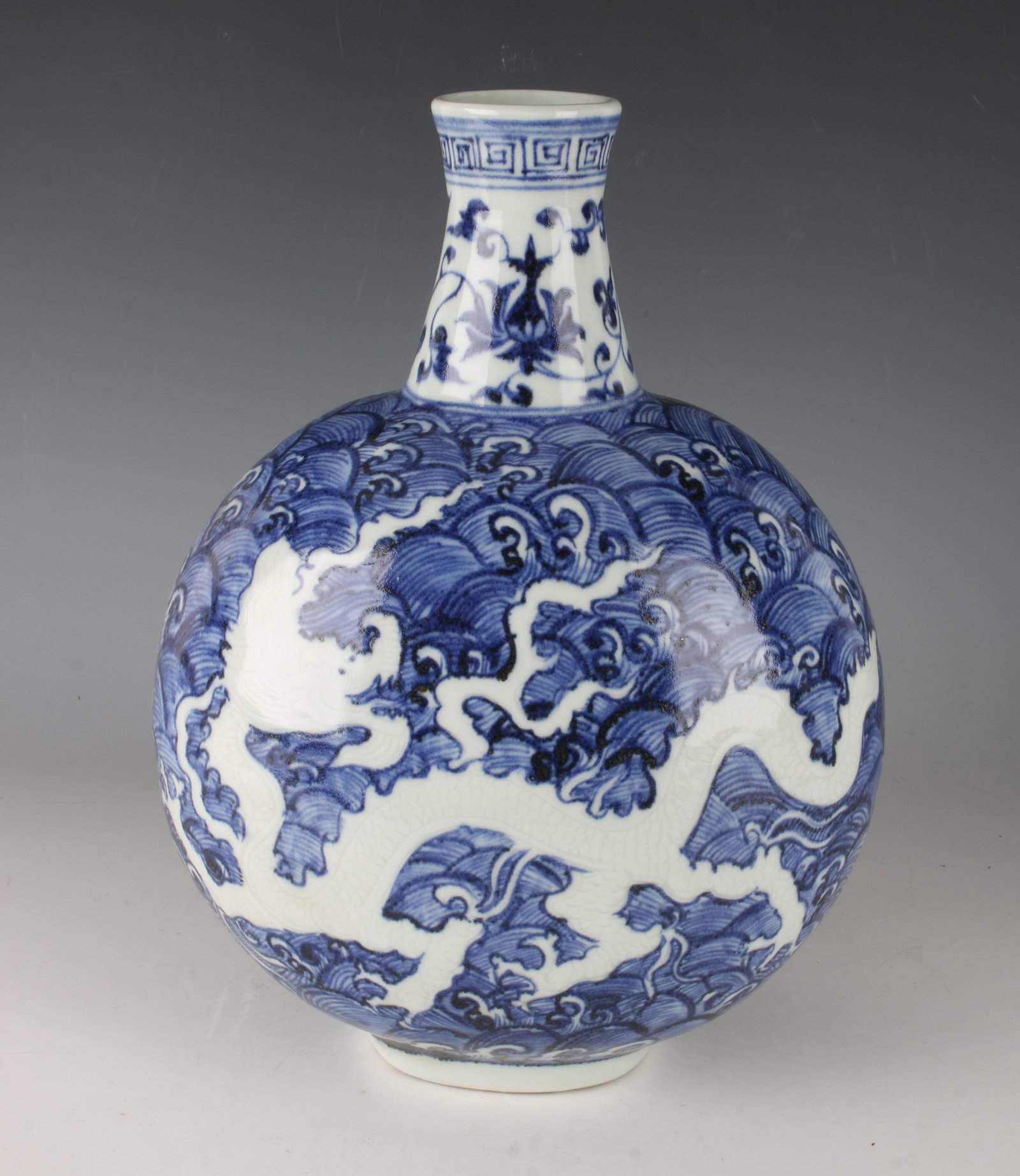 BLUE & WHITE REVERSE DRAGON MOON FLASK: BLUE & WHITE REVERSE DRAGON MOON FLASK: Meander border at the top over a flower and tendril border at the neck. Reverse dragon in blue waves. 8" X 12"