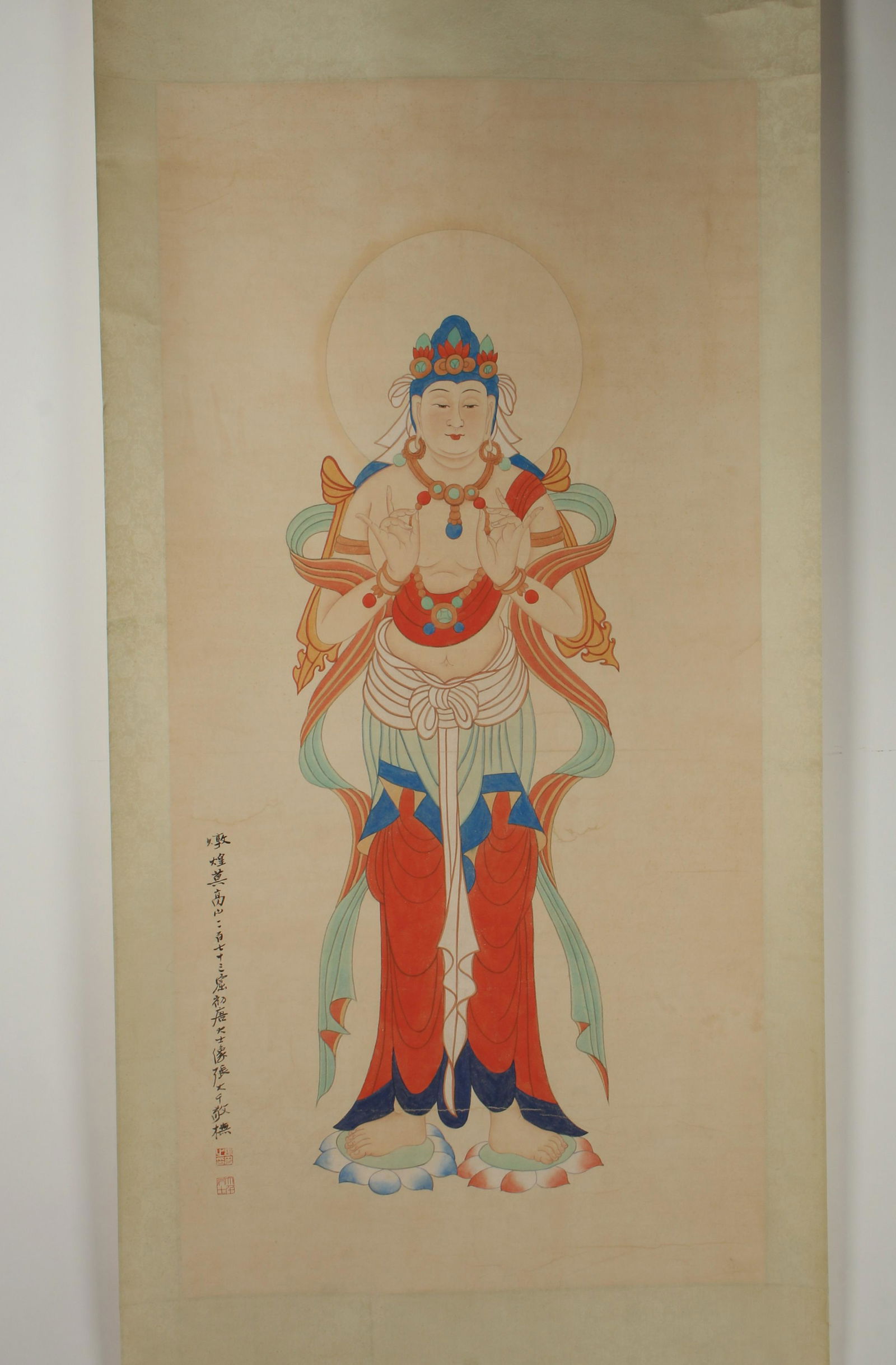 SCROLL OF ROBED BUDDHA: SCROLL OF ROBED BUDDHA: A Buddha stands on two lotus petals in colorful robes and jewels. Calligraphy and artist mark on left. 36 1/2" X 92" $400 - $600