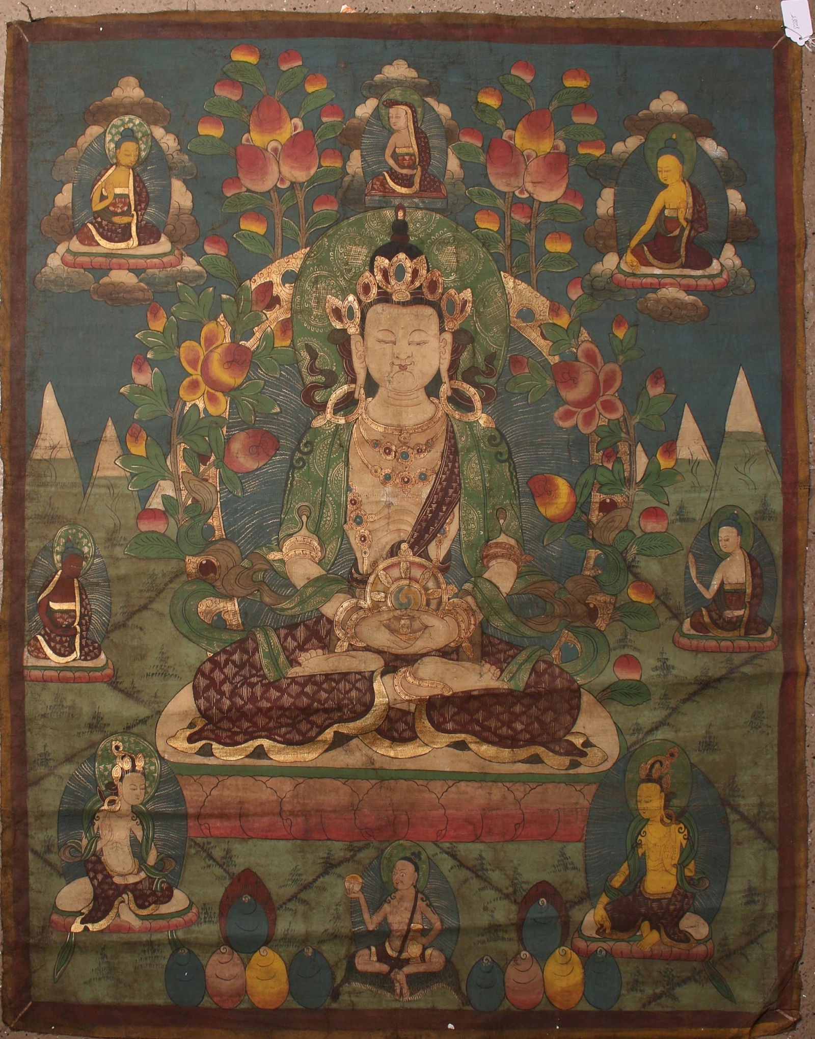LARGE SERENE BUDDHA & PEACHES THANGKA: LARGE SERENE BUDDHA & PEACHES THANGKA: A Buddha sits in the lotus position holding a large disc with a yin yang symbol in the middle draped in robes, jewels, wearing a headdress. He is surrounded