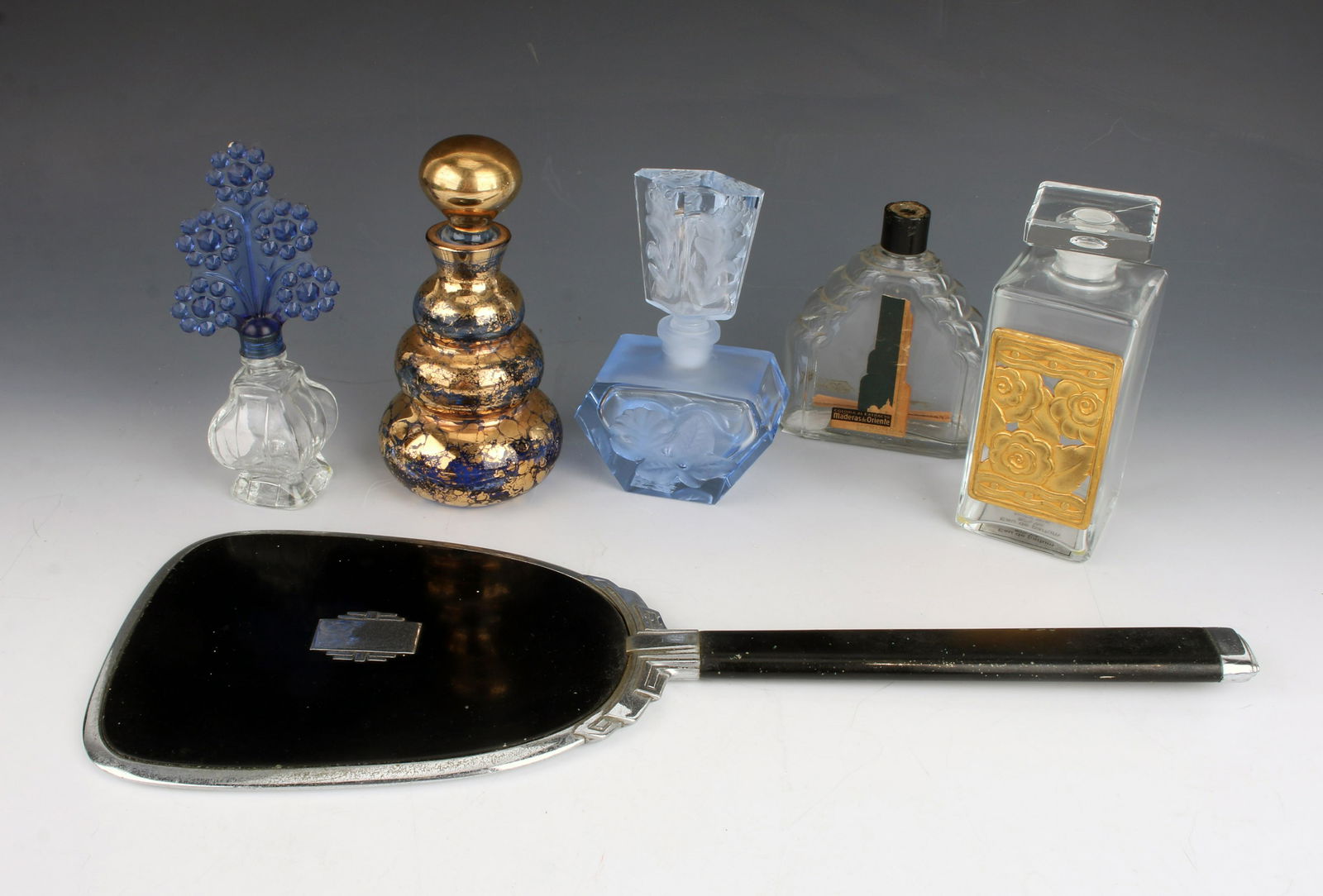 FIVE PERFUME BOTTLES & ART DECO HAND MIRROR: Vintage perfume bottles including a three tiered blue and gold glass marked 'Made in Hungary'. One is labeled "L'Aromarine". Hand mirror is beveled glass with black enameled back and handle.