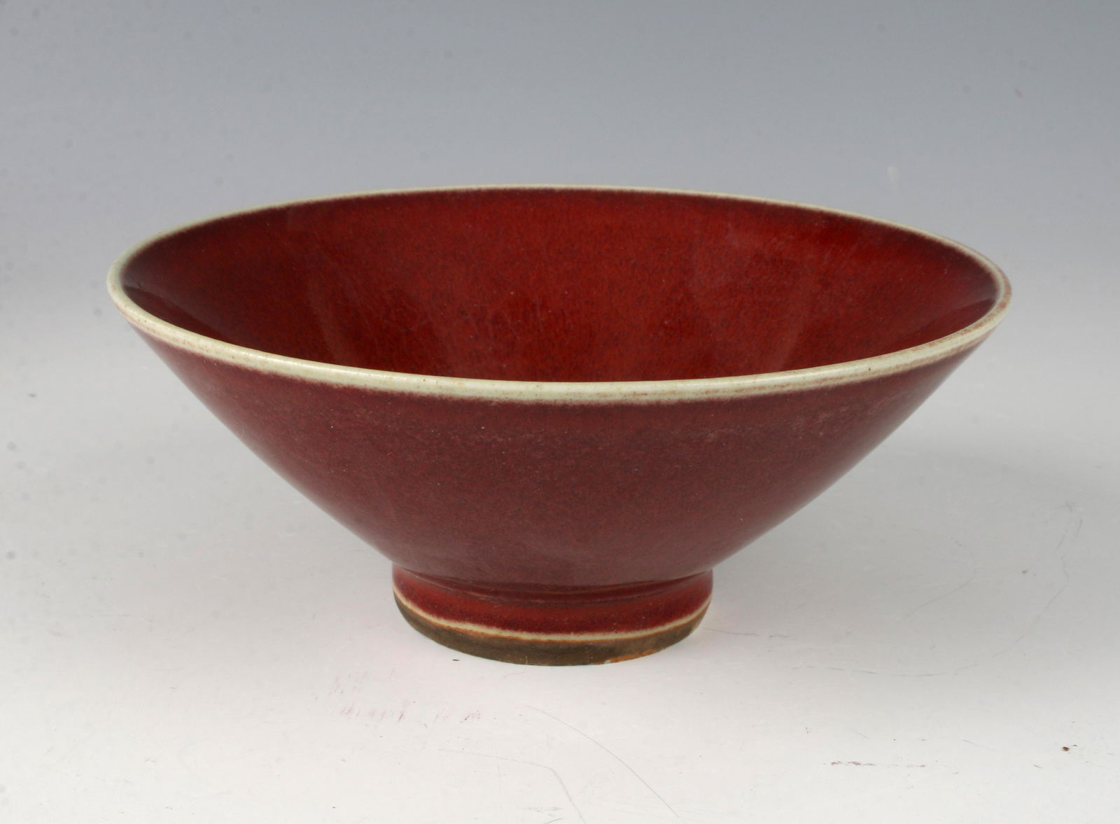 FLARED PORCELAIN OXBLOOD FOOTED DISH: Glazed in a faded oxblood with a small oil spot finish. On low unglazed foot. The bottom has a craquelure celadon decoration. 5" X 2" $200 - $400 Please contact us for high resolution