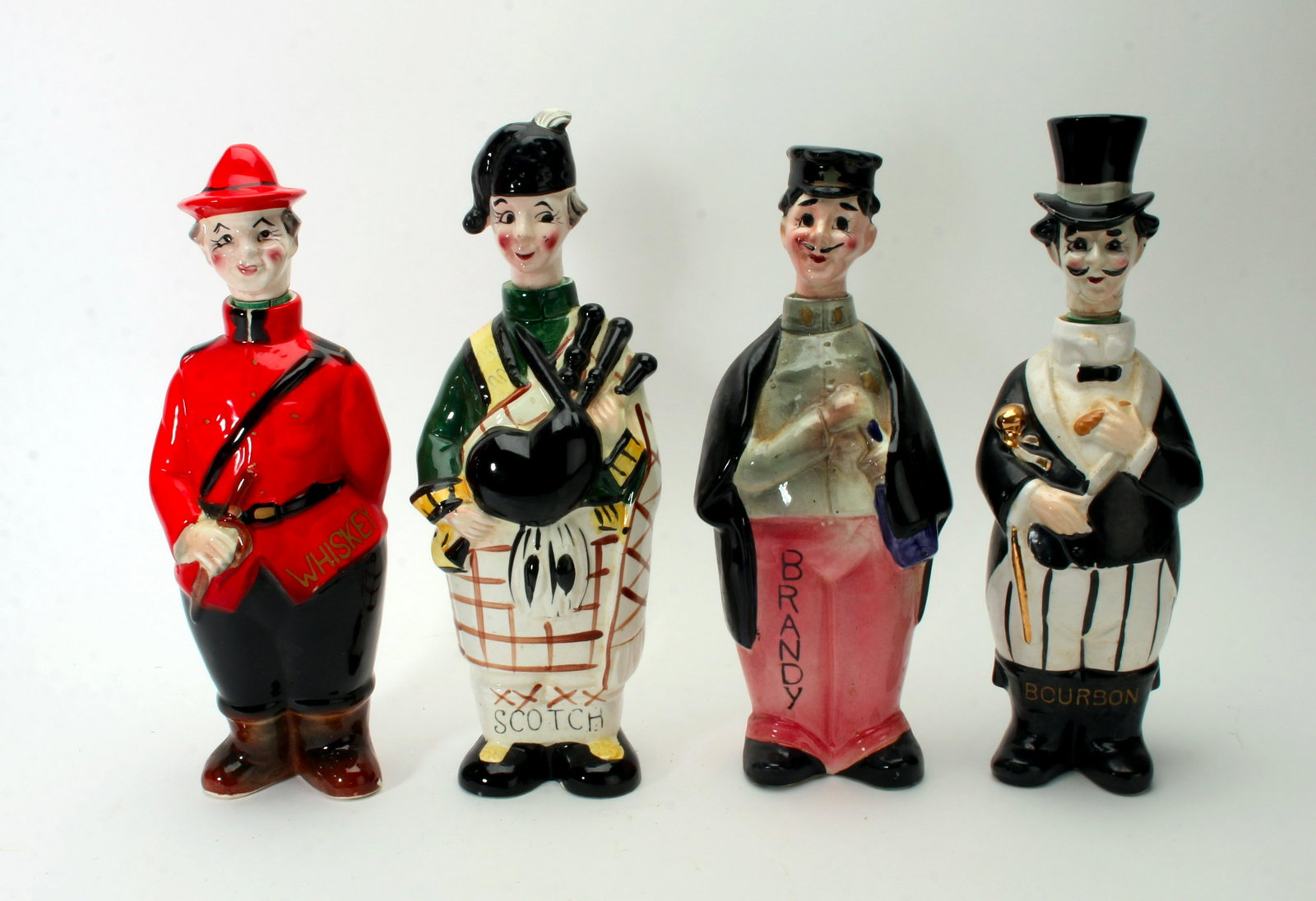 VINTAGE JAPANESE FIGURAL LIQUOR DECANTERS: Ceramic Whiskey, scotch, brandy, and bourbon decanters. Whiskey is dressed like a Canadian Mountie, Scotch is holding bagpipes, brandy is a Frenchman, bourbon is dressed in a top hat. Fill them to bri