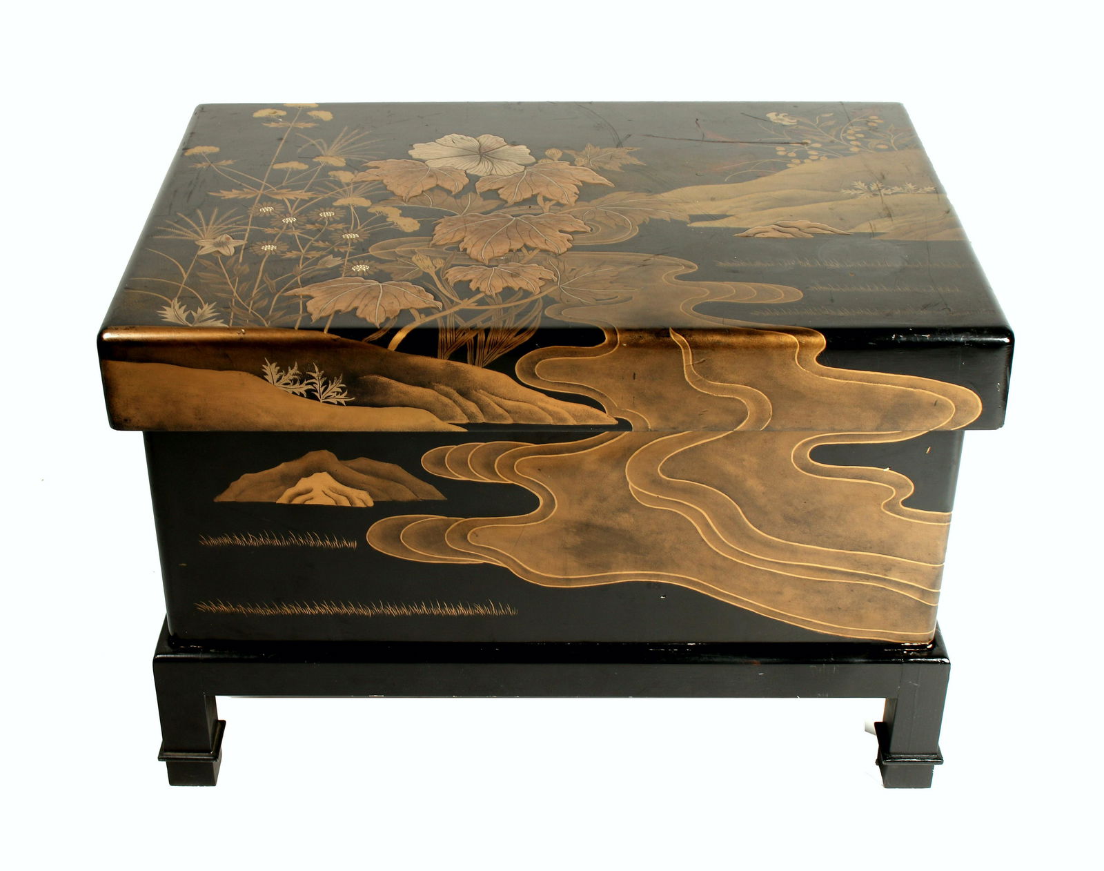 THREE PIECE LACQUERED CHEST: Makes a great coffee table, or extra storage. Three pieces; bottom stand, central box, and top lid. Various shades of gold on black background. The lid features plants along a river bank, the river fl