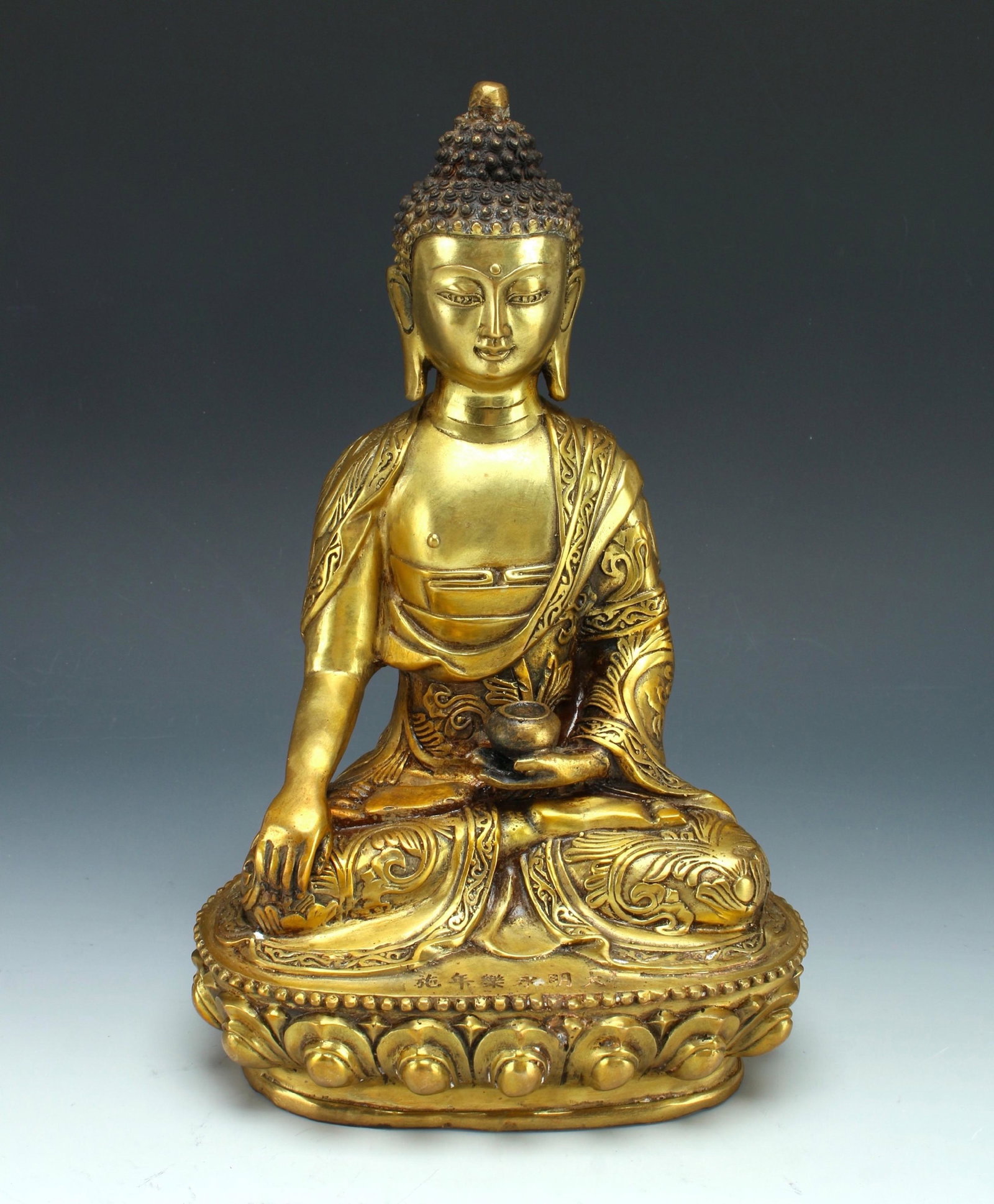 SEATED BRONZE BUDDHA: The Buddha is seated on a lotus pedestal draped in robes and holding a begging bowl. There are six characters on the pedestal in front of his legs. 7" X 11 1/2" $300 - $500 Please cont