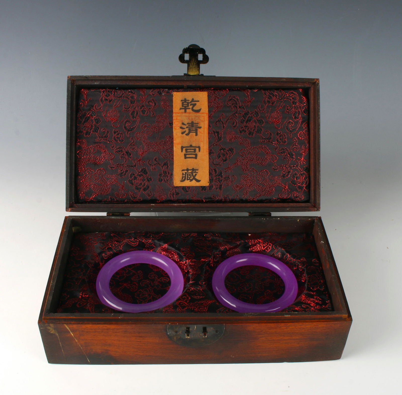 PAIR OF DYED LAVENDER BANGLES IN PRESENTATION BOX: Carved character marks all over with a plaque of four characters on the left with a bas relief central character. Red and black brocade inside and paper label with smooth dyed lavender jade bangles 2