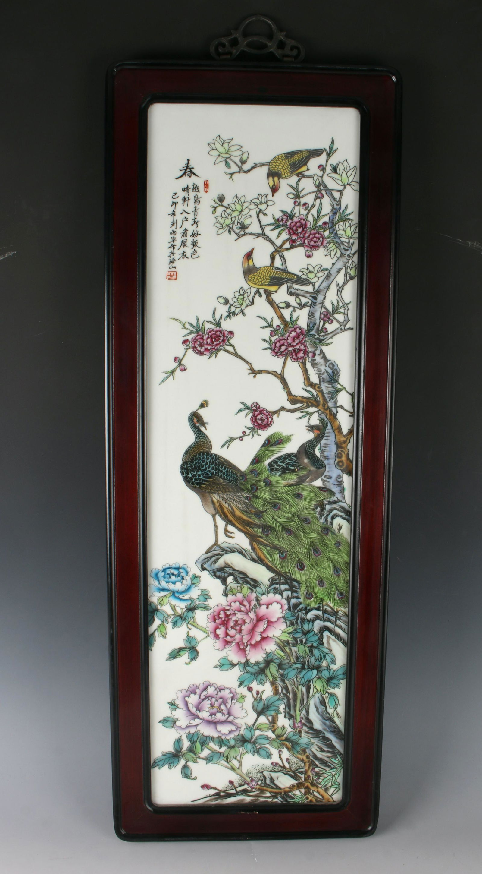 FRAMED PORCELAIN PEACOCK & FLOWER PLAQUE: A peacock and a peahen are perched on a boulder among colorful flowers with a pair of yellow song birds above. Calligraphy and artist mark on upper left. 11 1/2" X 34" $400 - $600 Ple