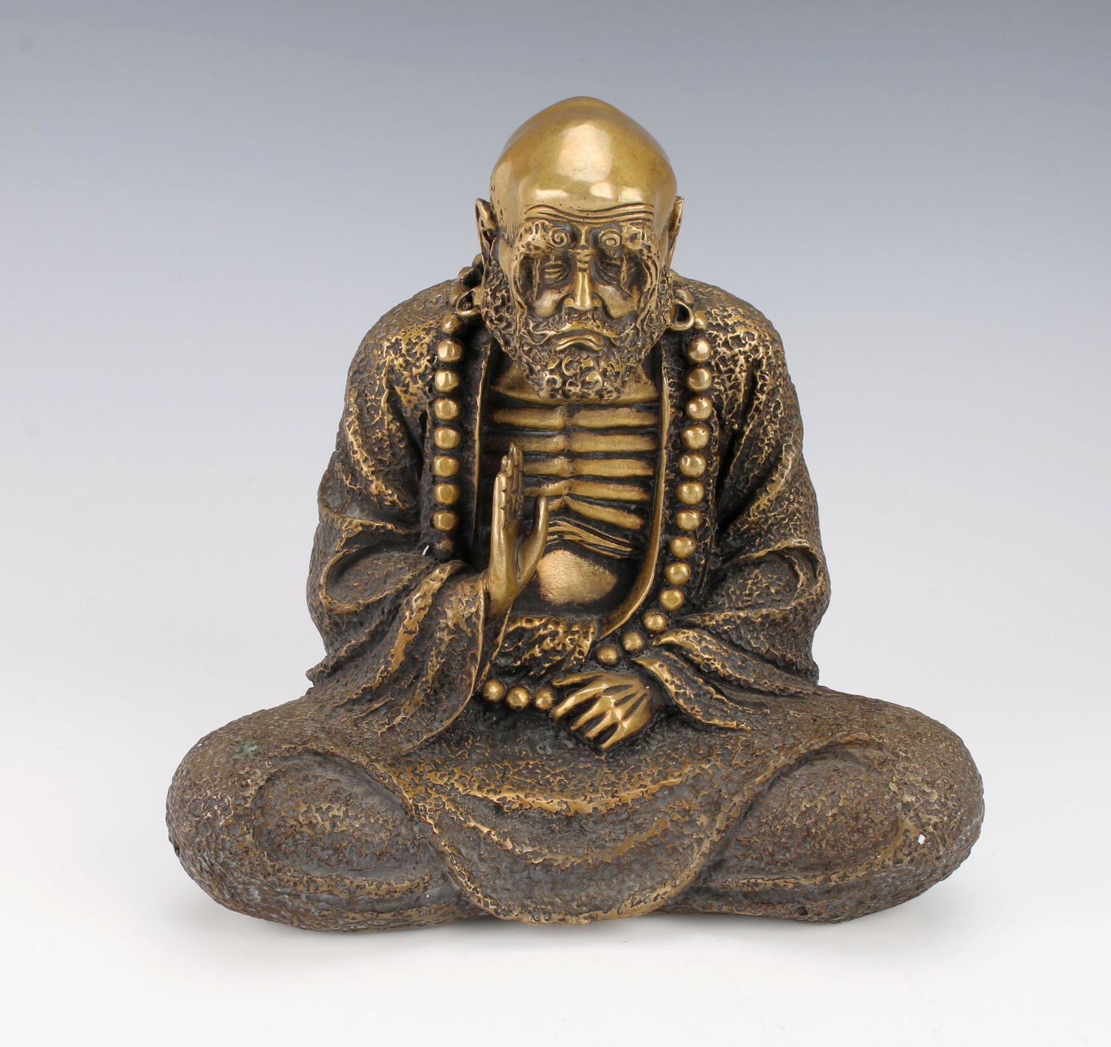 BRONZE BUDDHA STATUE: With weathered face and exposed ribs, he holds his one hand up with palm facing to his left. He wears a long beaded necklace and a long robe. 8" X 4" X 7 1/2" $300 - $500 Please