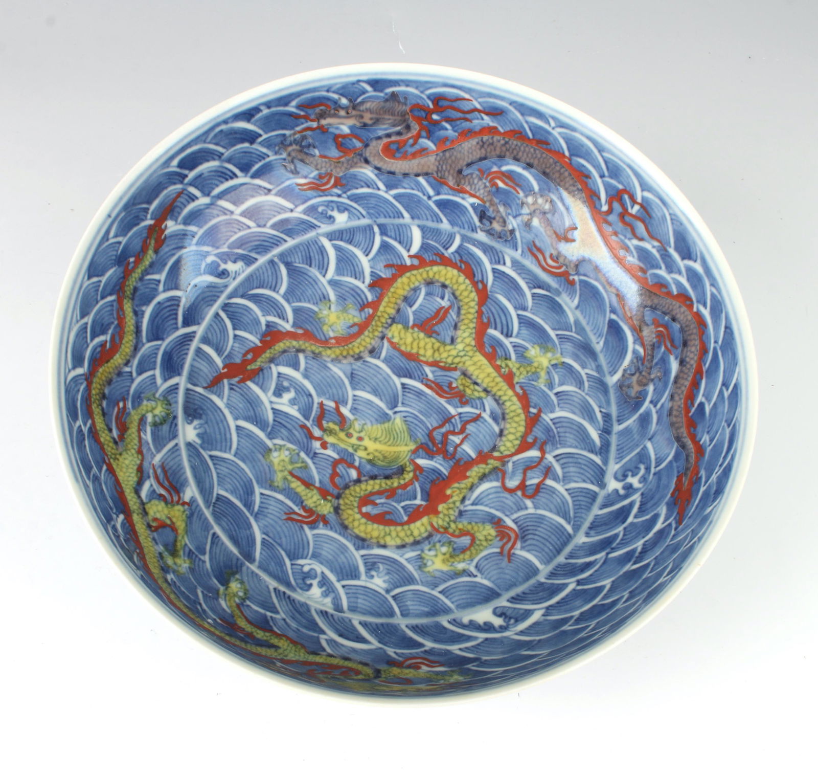 BLUE DRAGON BOWL: A yellow dragon is in the center of the bowl with two dragons surrounding it on a ground of waves. The outer rim is decorated with waves and dragons. Marked on the bottom. 9 1/4" X 2 3/4"