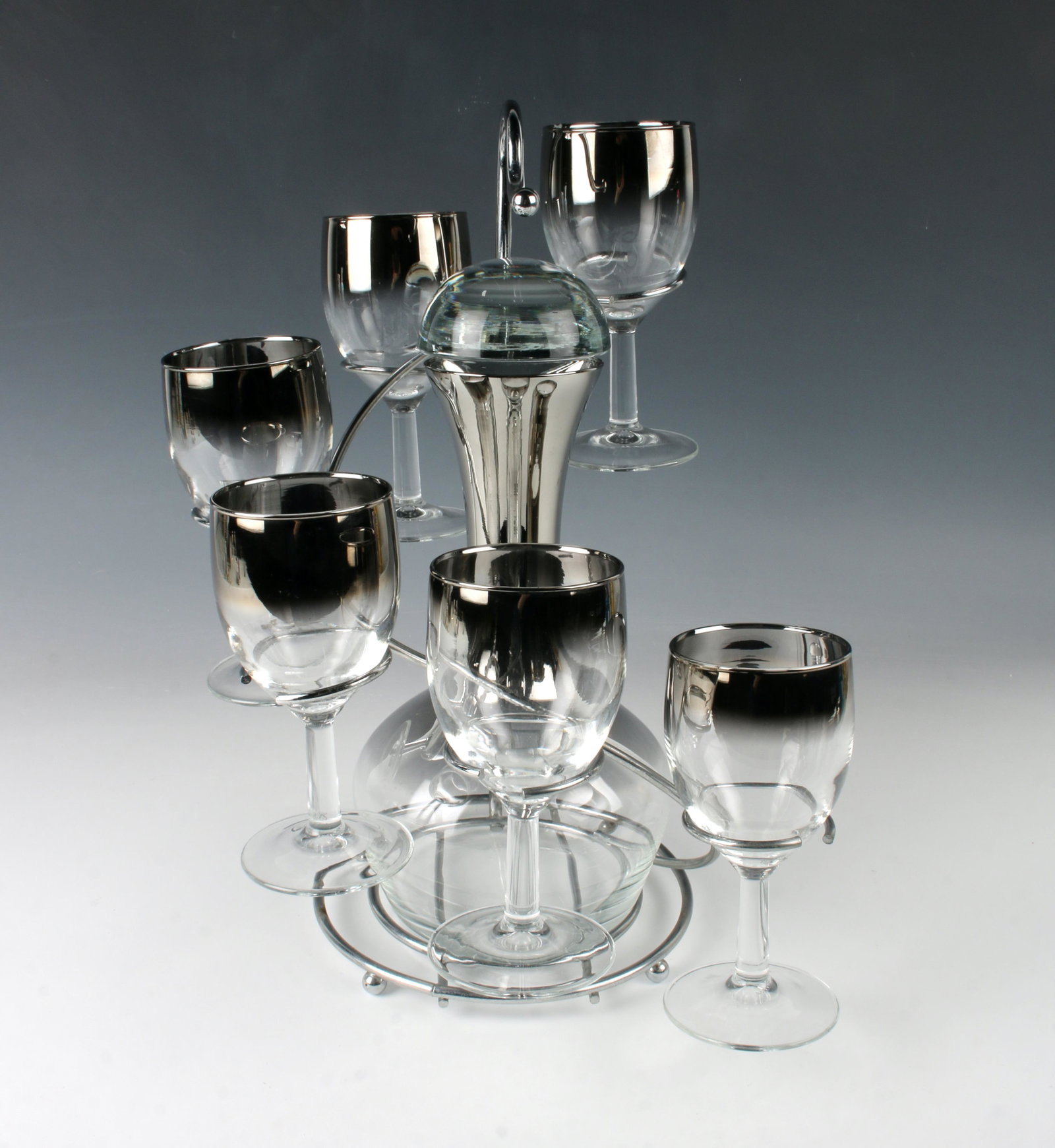 MCM SILVER FADE DECANTER SHERRY GLASSES W CADDY: Chrome caddy holds six sherry/small wine glasses and decanter. Glasses and decanter with silver fade effect that shows clear at the bottom. 9" X 12" $200 - $400 Please contact us for