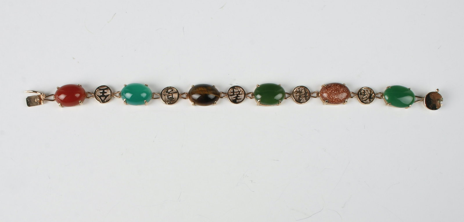 CHINESE JADE, TIGER EYE, CARNELIAN BRACELET: Alternating cabochon stone and character bracelet. Jade, gold stone, tiger eye, and carnelian. In gold tone. 7 1/4" $100 - $200 Please contact us for high resolution images of this lot.