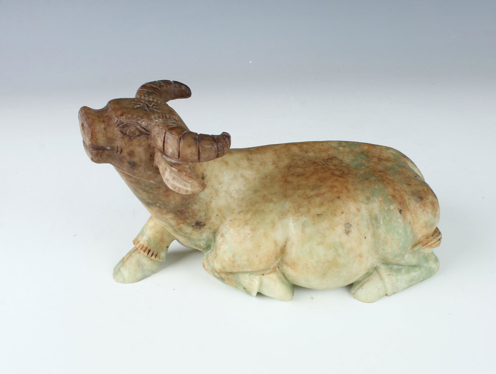 QING DYNASTY GREEN JADE WATER BUFFALO: A lounging water buffalo lays on its stomach with one hoof in front of him. His face and horns are detailed. Provenance: private local coll