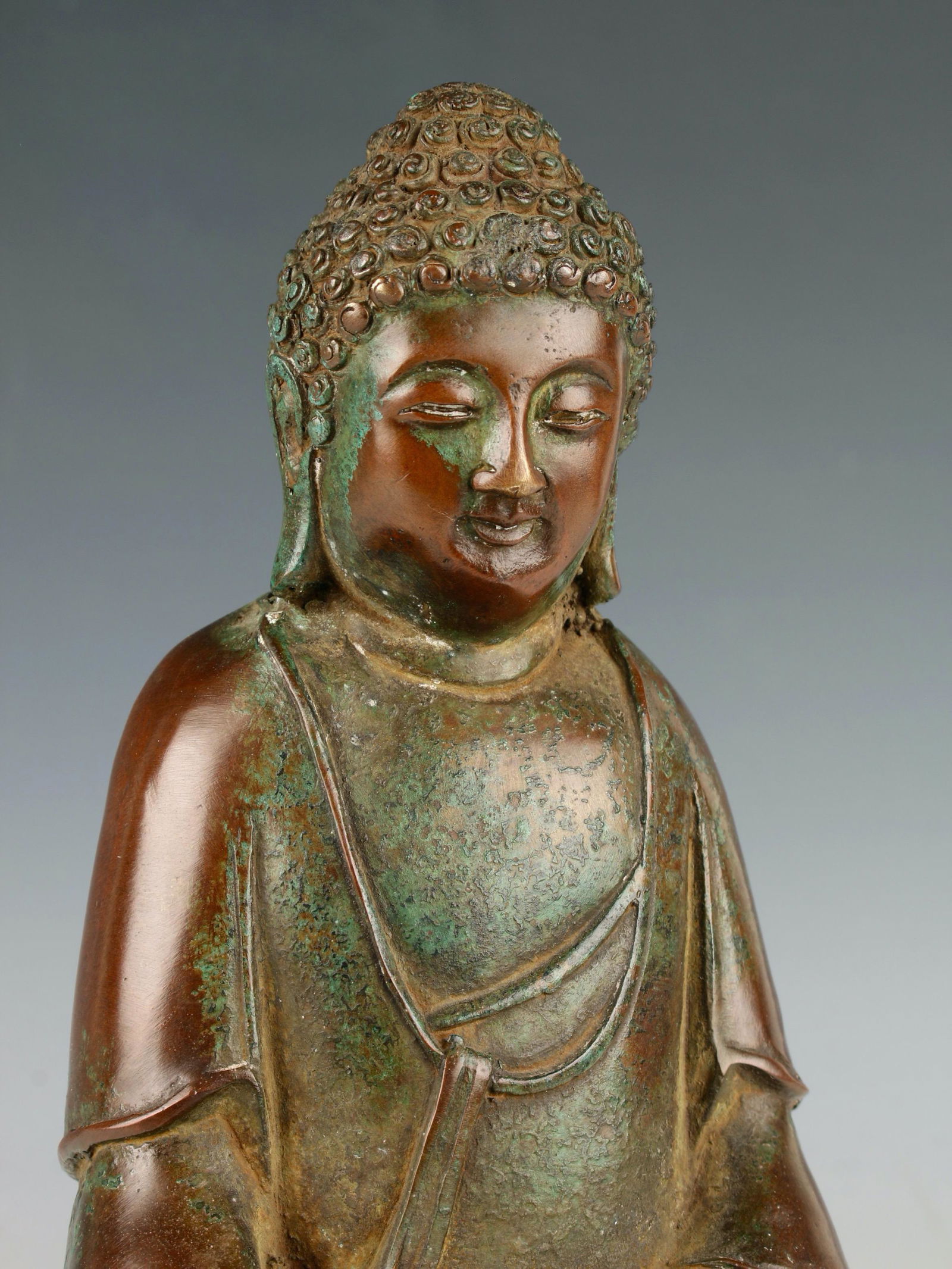CHINESE TIBETAN BRONZE BUDDHA: Antique Chinese Tibetan Bronze Buddha. In a warm brown and verdigris patina, the Buddha is seated on a stylized lotus pedestal mounted atop a hexagonal plinth. The right hand faces upward while the le