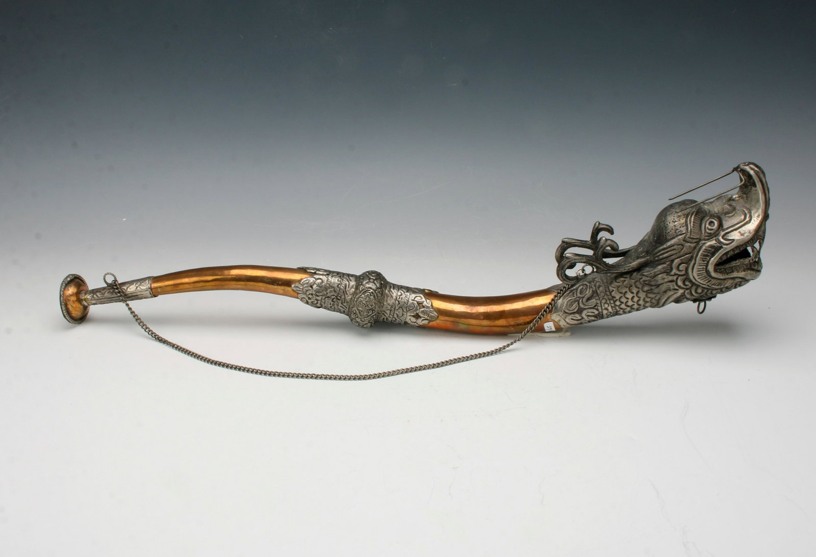 COPPER & CHINESE SILVER DRAGON HORN NEPAL: The open horn is in the form of a dragon's mouth. Embossed metal work all over. With chain for hanging 20" X 2" $200 - $400 Please contact us for high resolution images of this lot.