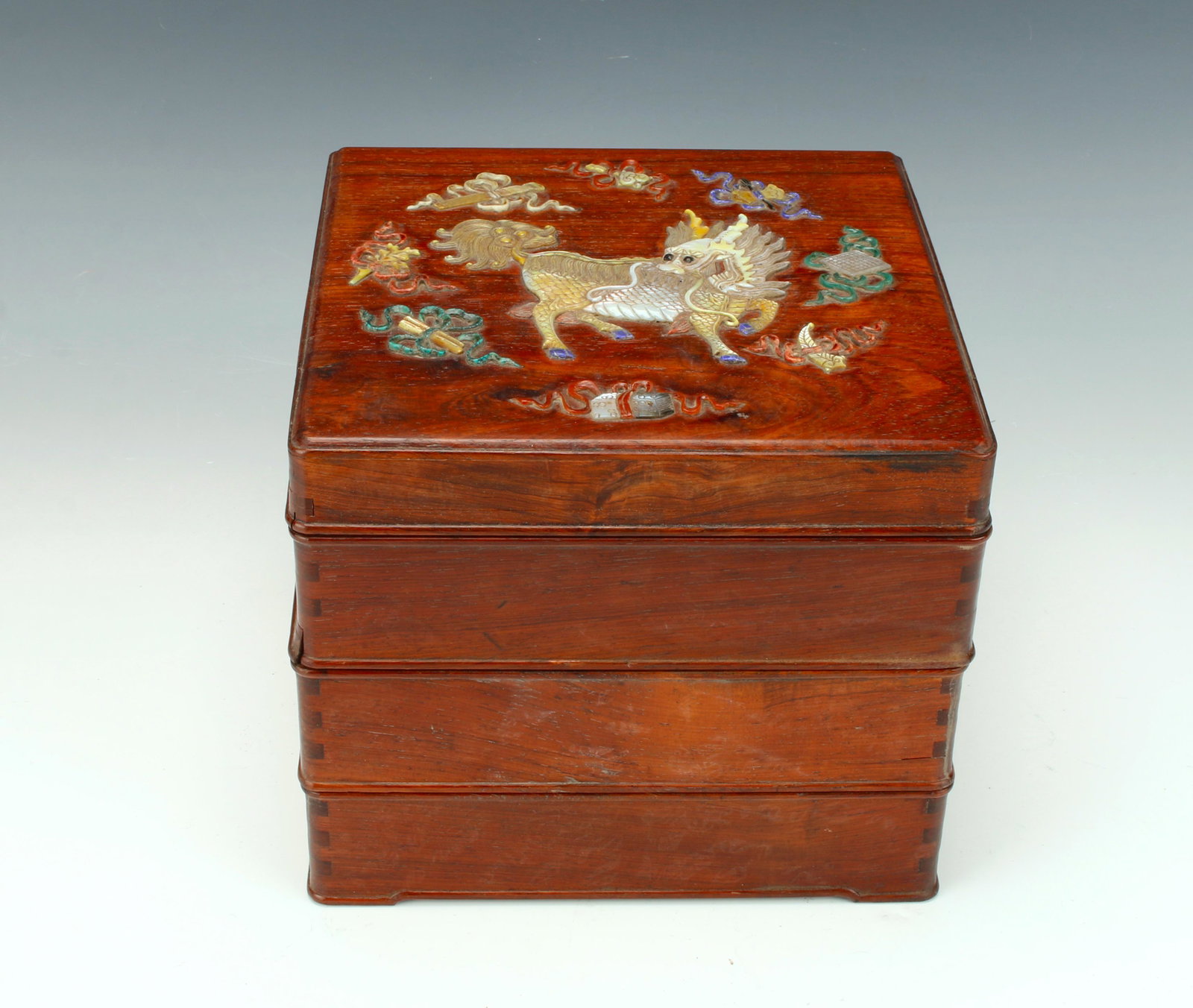FOUR TIERED APPLIED HARD STONE HUANGHUALI BOX: A kirin is on the lid surrounded by scholar's items. Box in four tiers with four raised feet on the bottom. Provenance: private collection.