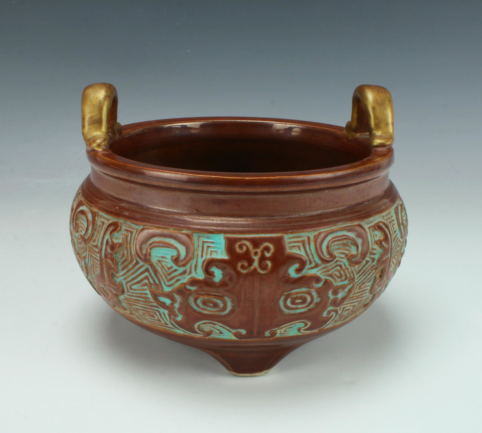 ARCHAIC FORM TRIPOD PORCELAIN CENSER: Glazed brown with gold loop handles and verdigris colored accents on tripod feet. Marked on the bottom. 6 1/2" X 5" $300 - $500 Please contact us for high resolution images of this lot