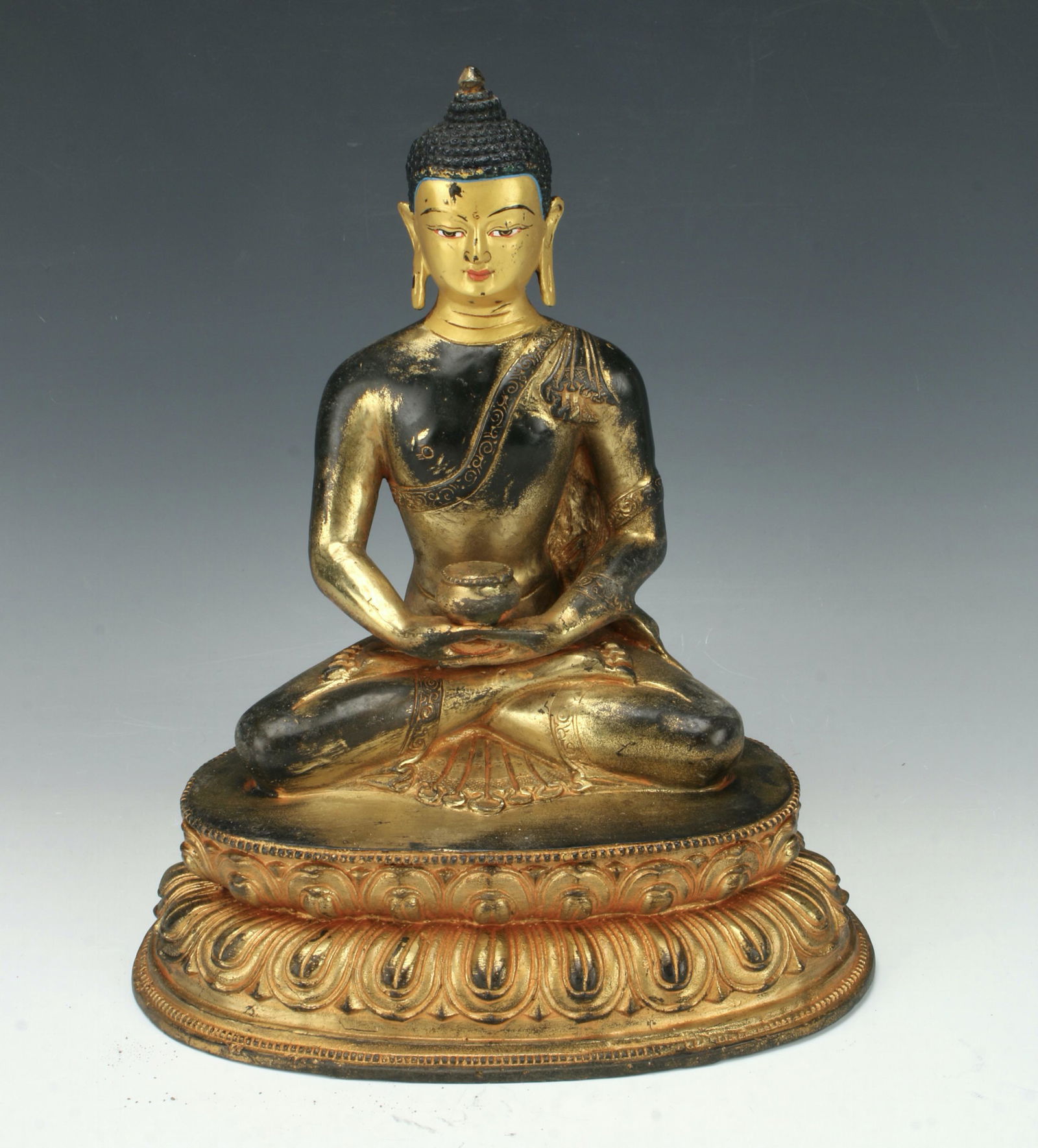 BRONZE BUDDHA WITH BEGGING BOWL: Seated in the lotus position on a lotus pedestal. Holding a begging bowl in both hands. Elongated ears and grape hair with a robe draped over one shoulder. Proven