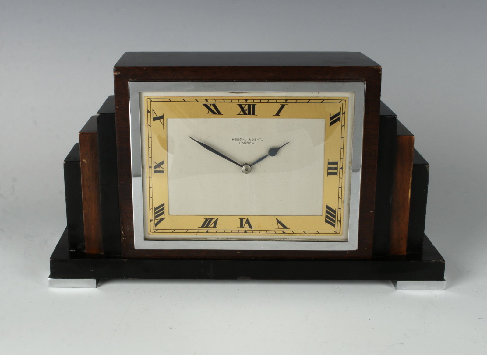 KENDAL & DENT LONDON ART DECO DESK CLOCK: Classic Art Deco styling with architectural stepped wood form alternating between black and brown wood. With a brushed silver face surrounded by gold chapter ring with Roman Numerals. 10" X 5 1/2