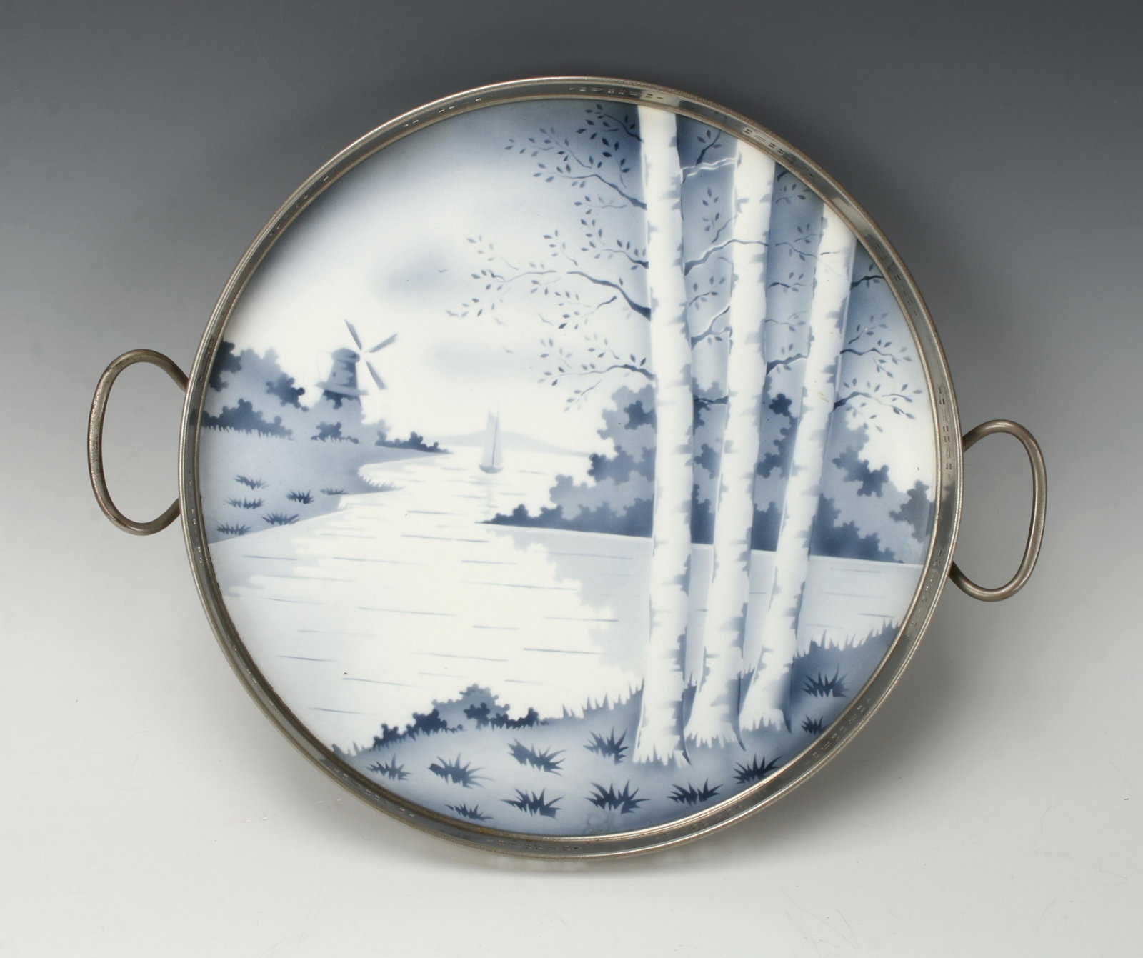 VINTAGE DELFT CIRCULAR TRAY: Hand painted circular scene of a canal with birch trees in the foreground, windmill and boat in the background. Set in pierced metal rim and handles. Back is marked 1 Y 2 8, 5042. 14" $40 - $8