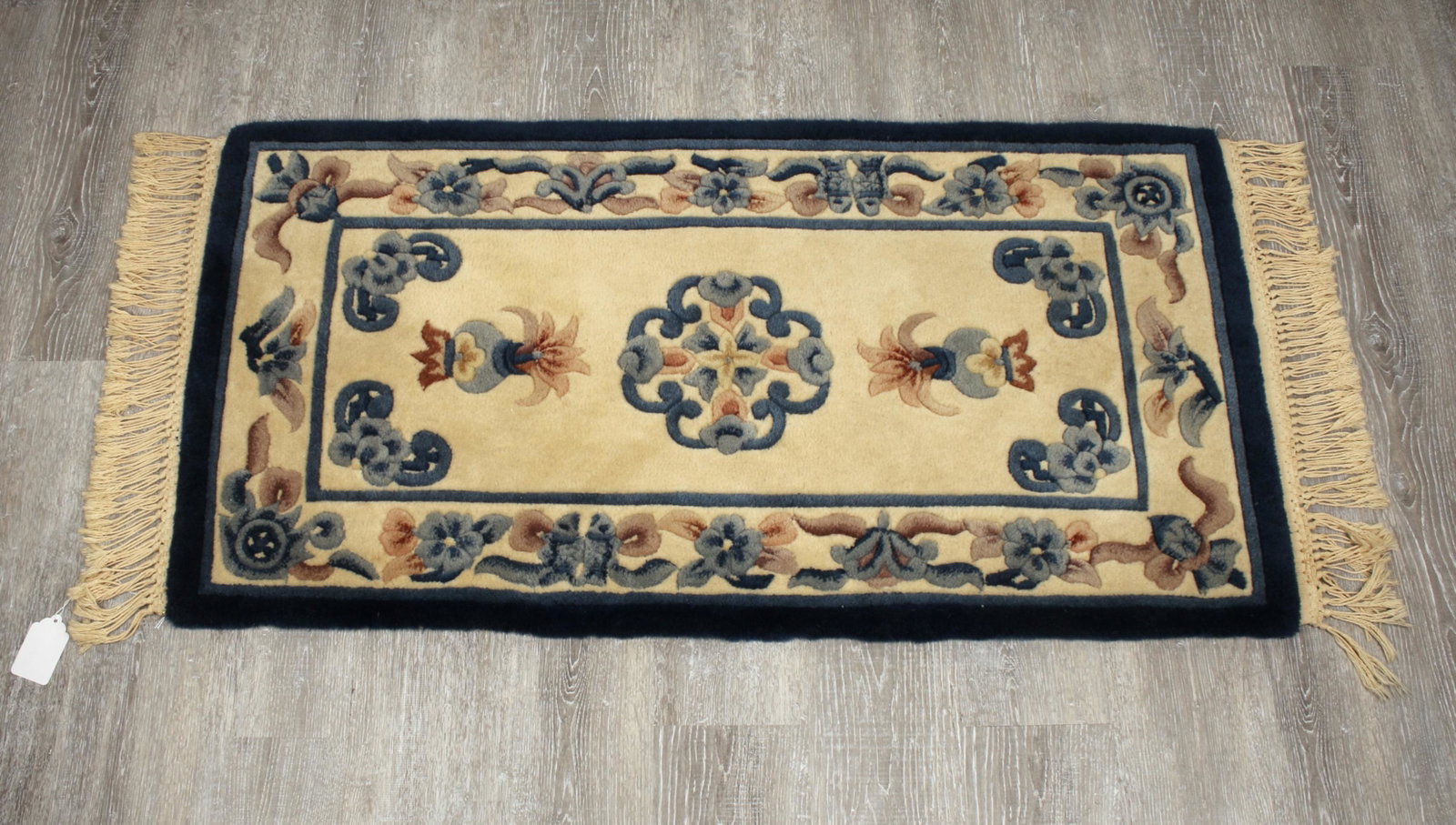CHINESE WOOL FLORAL AREA RUG.: Floral motifs in blue and beige. Central is a vase with flowers surrounded by scholar's items. Label on back indicating all wool rug handmade in China. 48" x 24" $200 - $400 Please co
