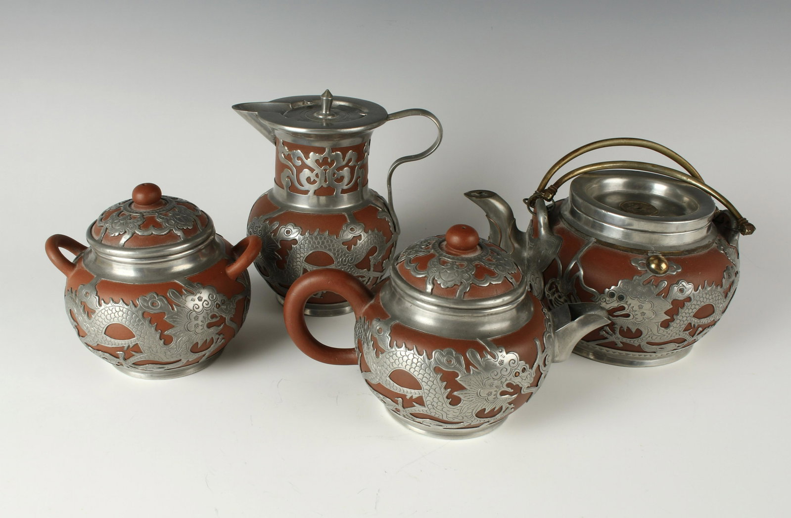 4 PIECE YIXING RED CLAY TEA SET: Including tea pot, hot water pot, sugar, and creamer. Dragon pewter with red copper eyes. Applied pewter spout. Red clay lid with knob pierced with steam vent and pewter mounts of butterflies. 5 1/2&q