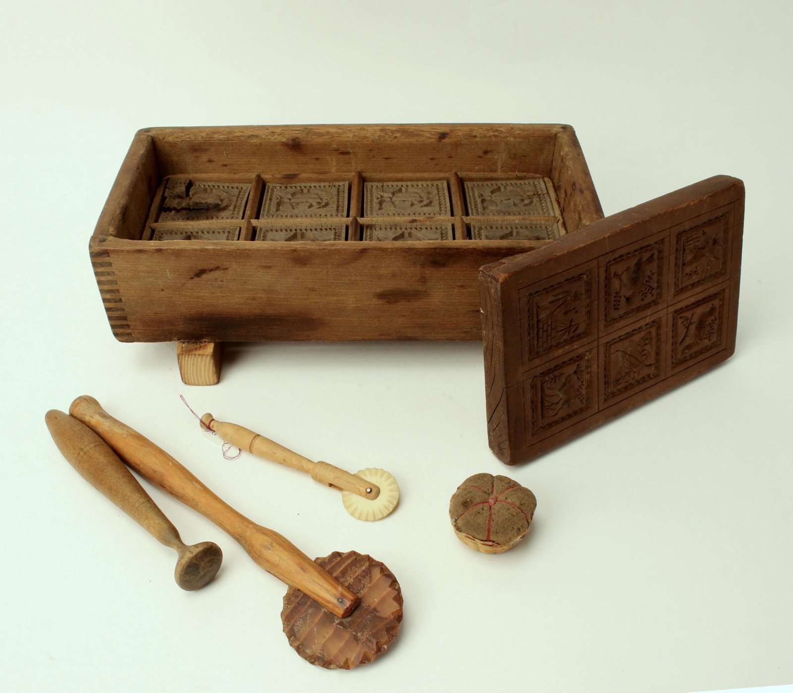 BOX OF WOODEN BUTTER MOLDS, CRIMPERS, SHAKER: Two early butter molds, Shaker pin cushion, 2 pie crimpers. Larger one is in a rectangular wood mold monogrammed and edge border. The other is six square images carved on a single piece of wood with b