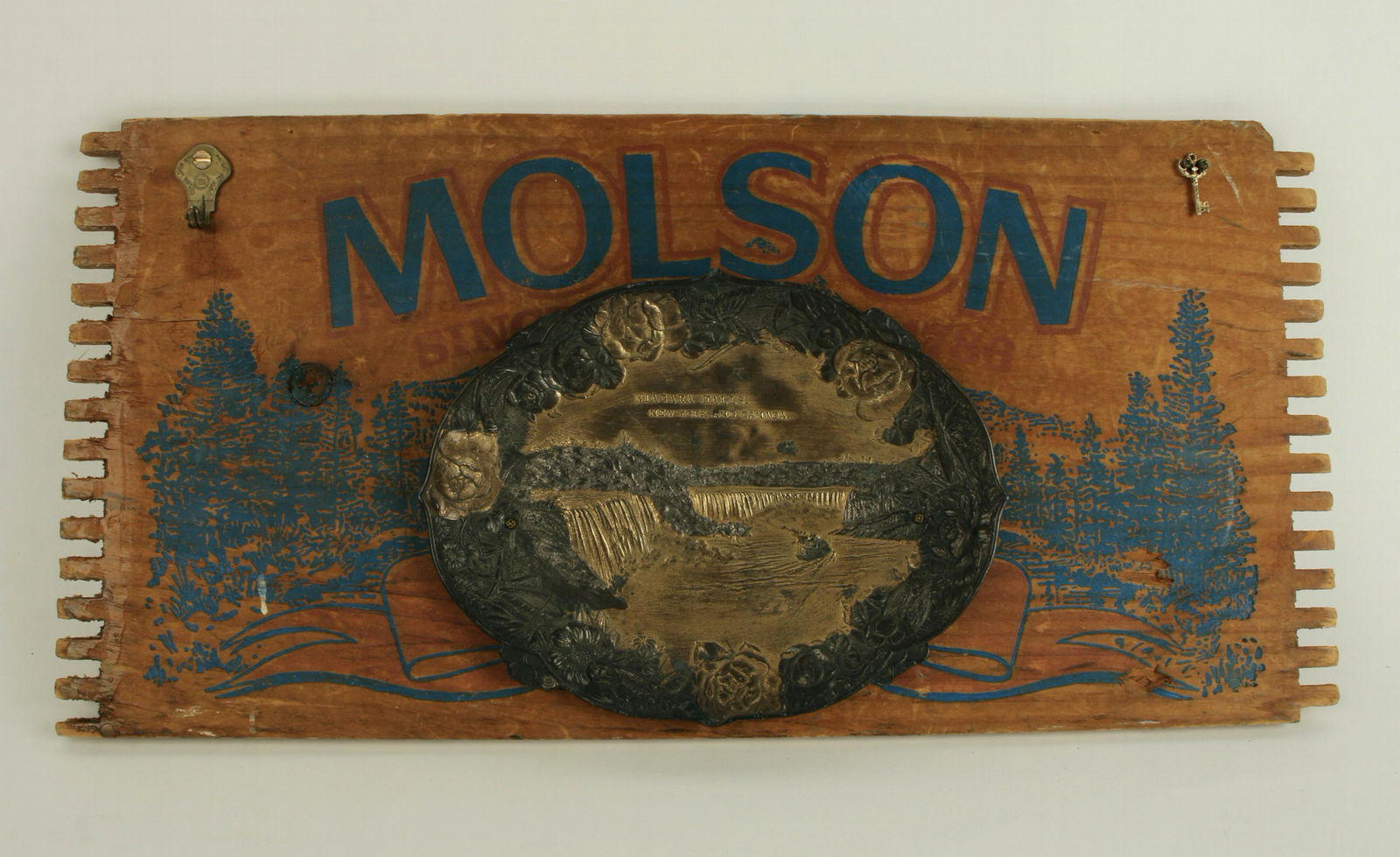MOLSON NIAGARA FALLS WOODEN SIGN: A Molson crate serves as a background as an assembled plaque with a Niagara Falls metal dish attached. Key formed in to a hook on left, small key on right. 18" X 8 1/2" $40 - $80 Plea