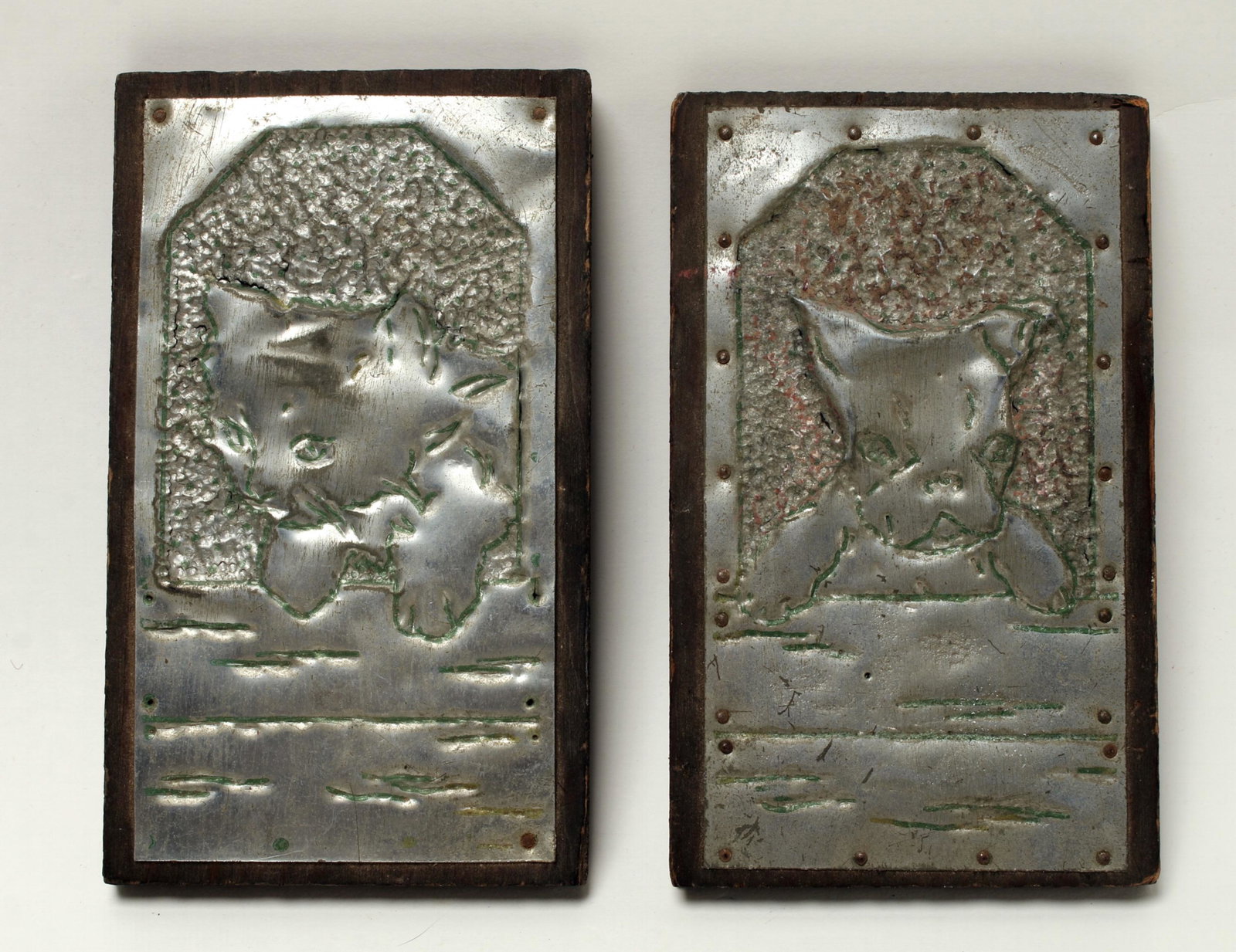 TWO VINTAGE FOLK ART CHASED CAT & DOG PLAQUES: Charming tin art depicting a cat on one, and a dog, both looking out of windows. These are hammered from the back of the metal to achieve a 3D effect. 3 1/2" X 10" $20 - $40 Please con
