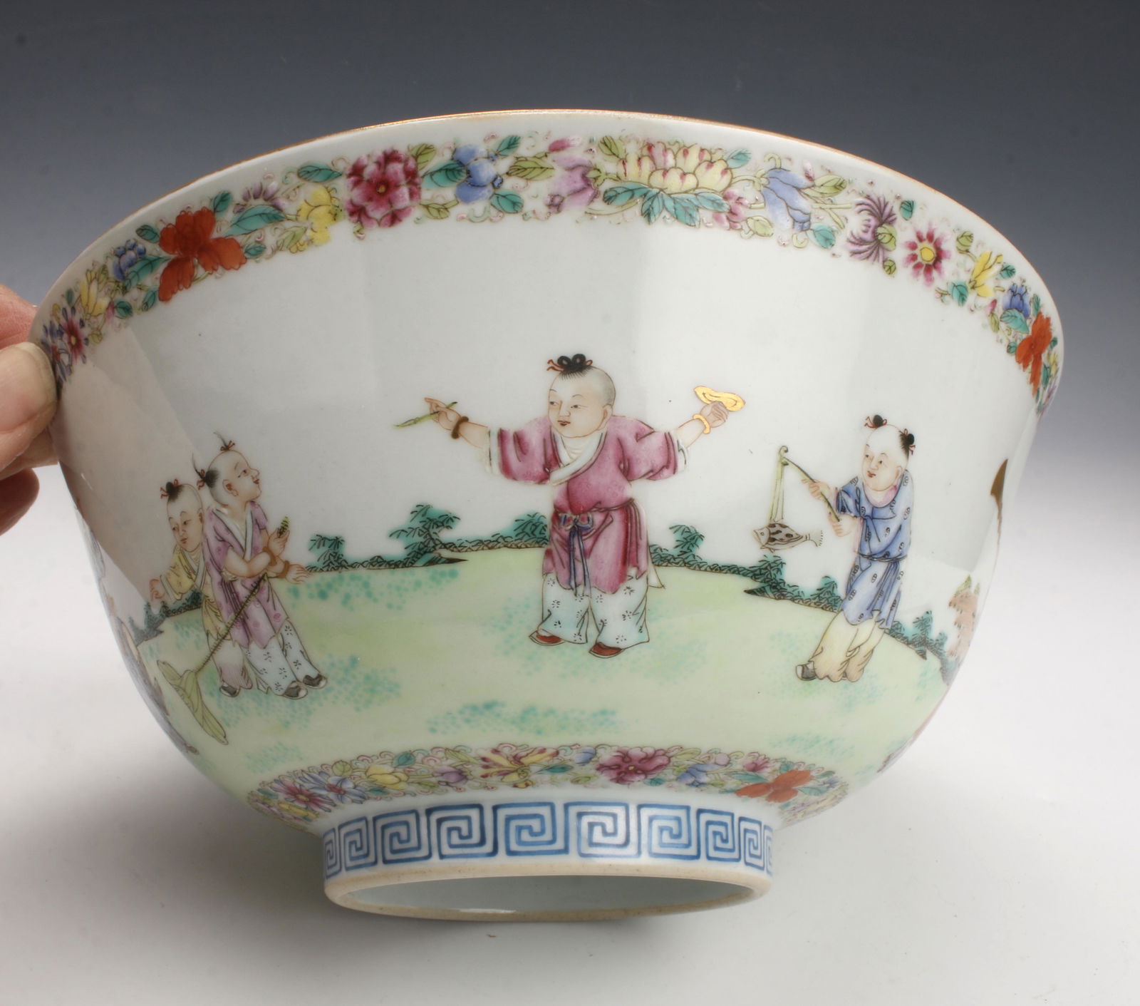 SCENIC PORCELAIN FAMILLE ROSE BOWL: Intricately painted multicolor bowl of an outdoor scene. Children are playing in a garden with banners, instruments, and games. Accented in gold. Marked on the bottom. In presentation box.