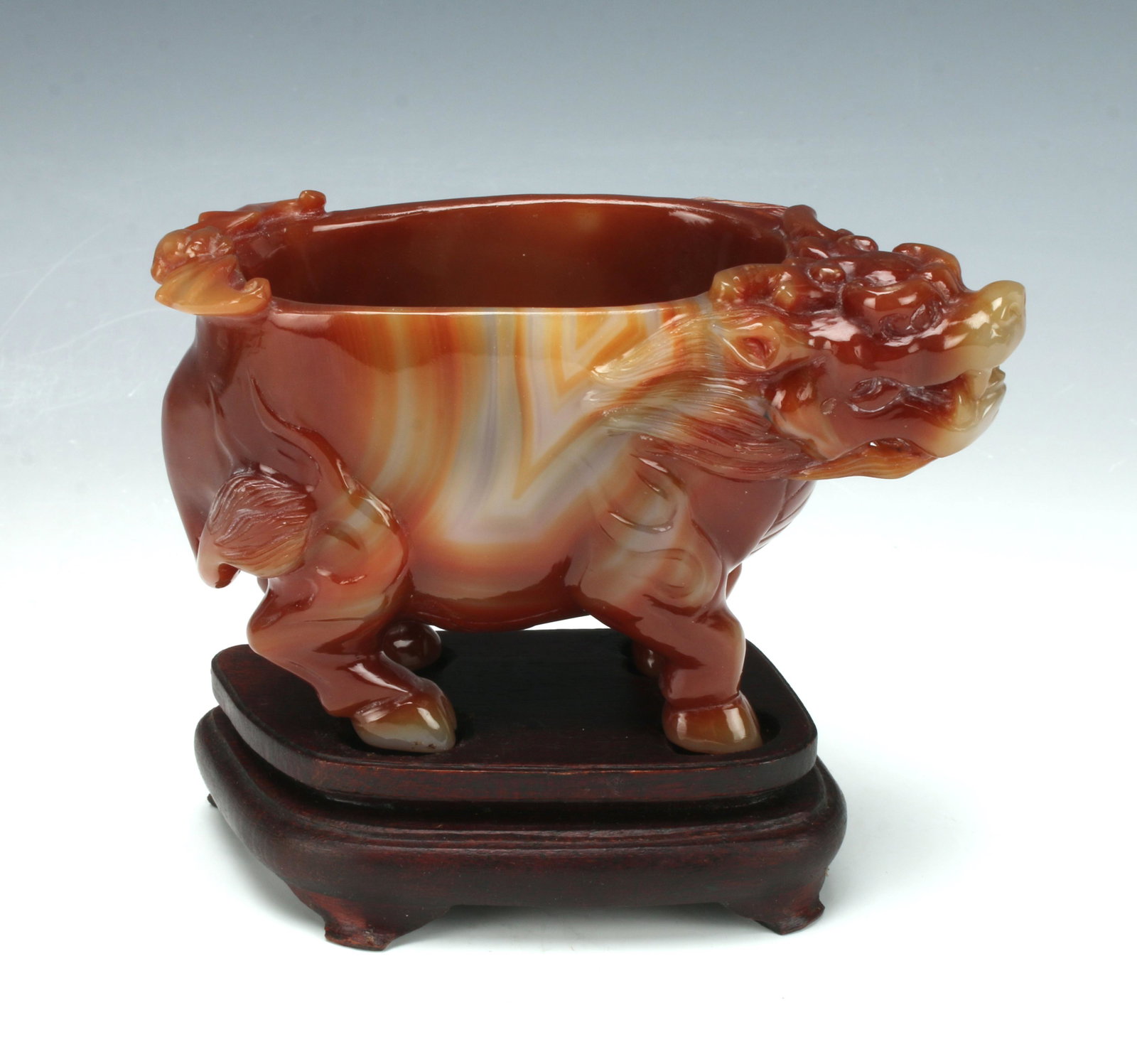 CARVED AGATE BEAST FIGURE ON CUSTOM STAND: A carving of a beast in agate in a bowl form. Hoofed feet, a tail, ears, and sharp teeth. On custom stand 5" X 4" $200 - $400 Please contact us for high resolution images of this lot.