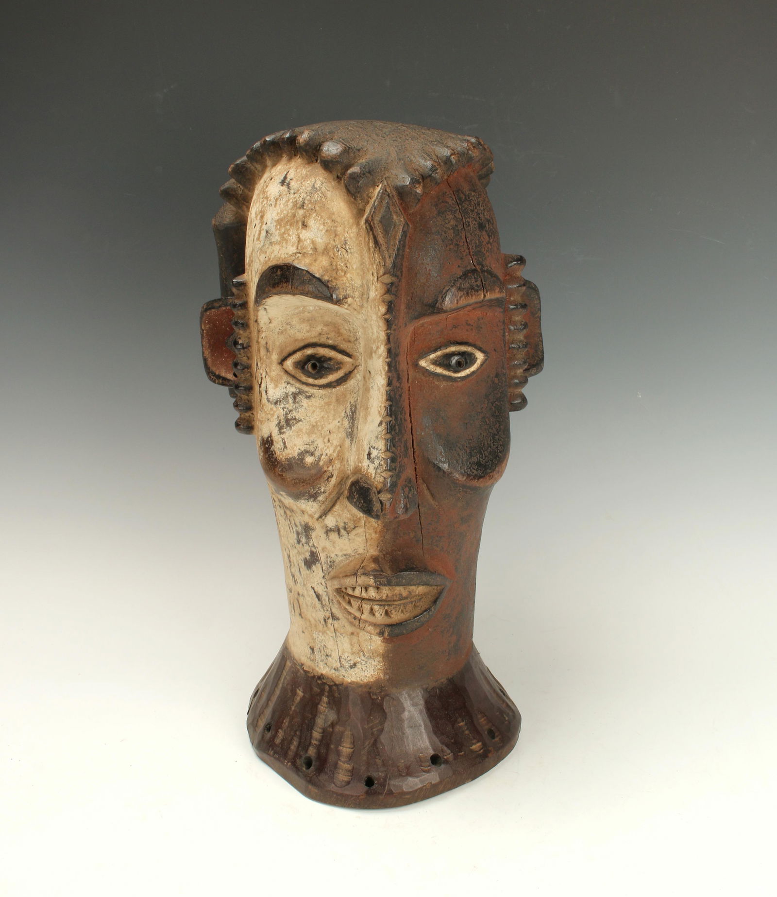 AFRICAN IKANGA HELMET MASK NIGERIA: Tall face form mask in half white and half red. High cheekbones, elongated nose with carved ridges, protruding lips with detailed carved teeth. Black eyes are bordered in white and black. Black brows,