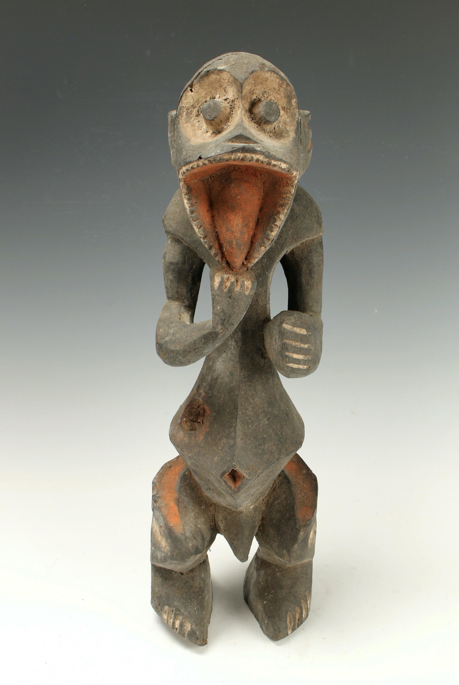 MAMBILA FETISH STATUE NIGERIA: Painted in black with white and red accents. Heart shape face with white eye sockets and open mouth revealing large tongue. Both heads have protruding eyes and tongue sticking out. Belly protrudes wit