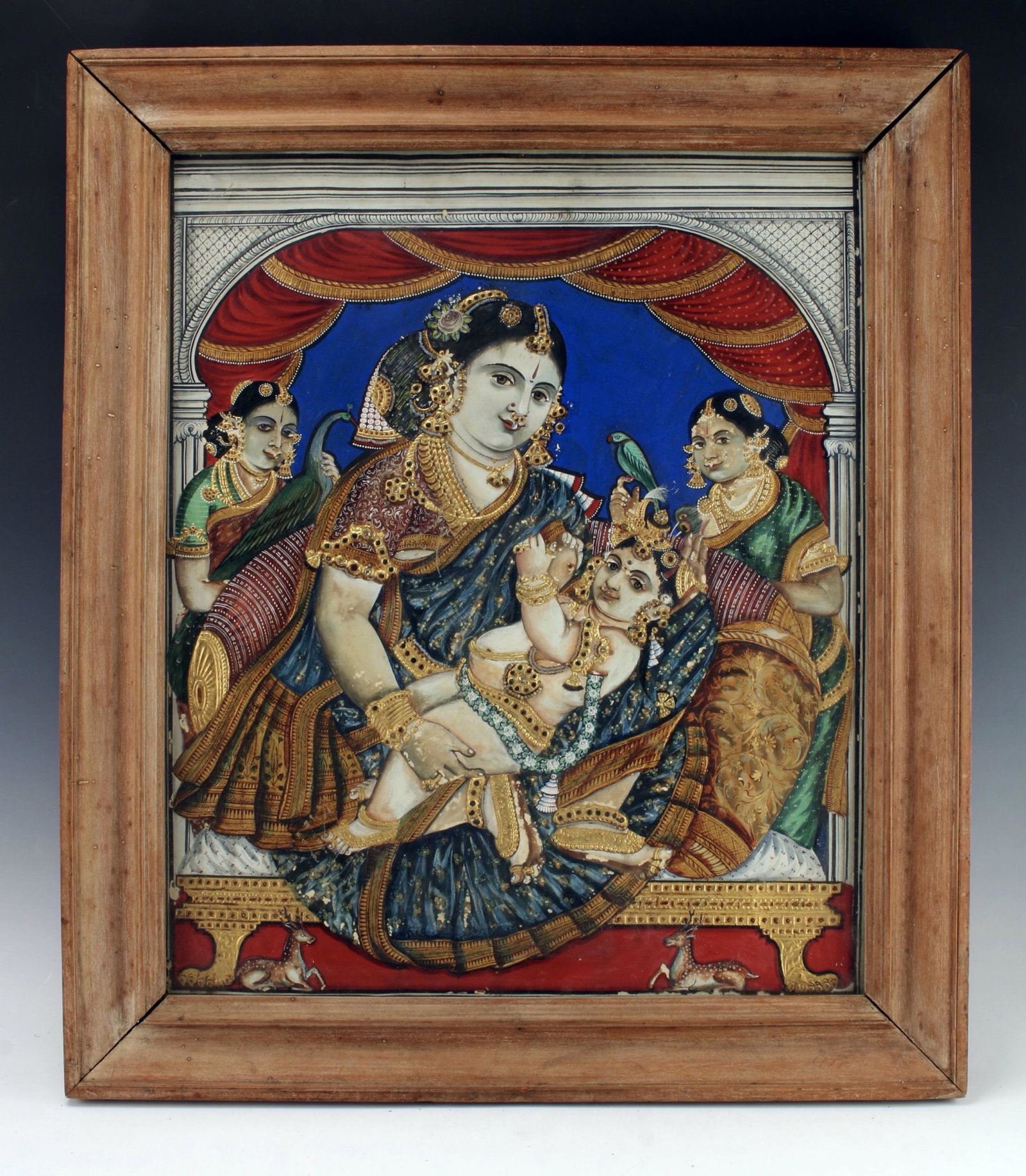 DIMENSIONAL PAINTING INDIAN GODDESS PAINTING: A three dimensional painting of an Indian goddess holding a baby with an attendant on either side. The goddess is seen in a theatrical backdrop of gold and red curtains. In an architectural frame. One