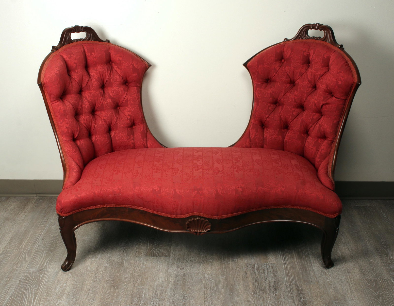 RARE SHAPED VICTORIAN LOVE SEAT: Single bench seat with two curved, tufted backs. Designed for intimate conversation. Carved handle forms on back of each seat, carved shell on front apron. Upholstered in dark red brocade. 45" X 