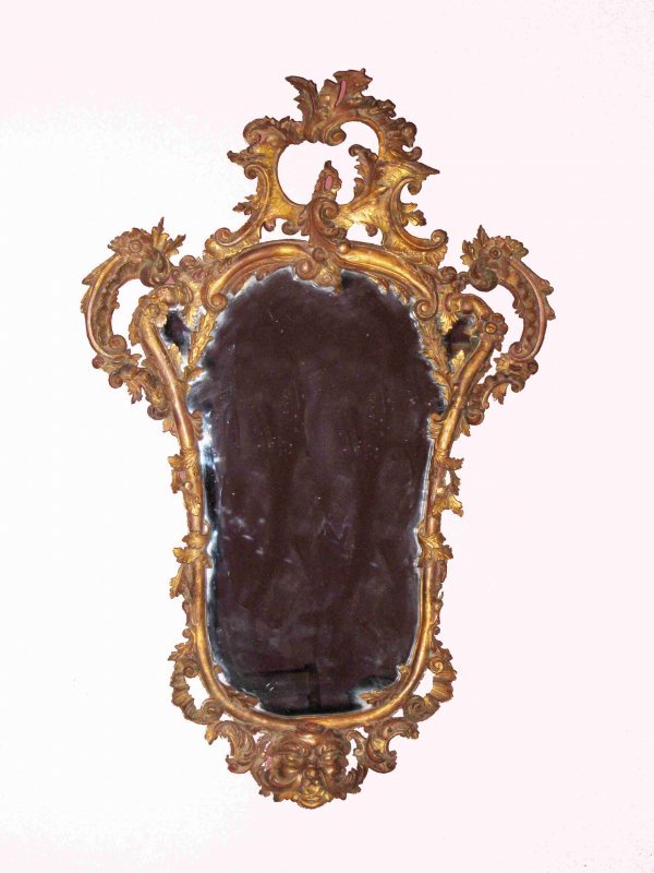 Carved Giltwood Mirror: A carved giltwood mirror in the Baroque style. The mirror frame is hand carved and with age that would have us think its over 100 years old. The glass is likely a later replacement