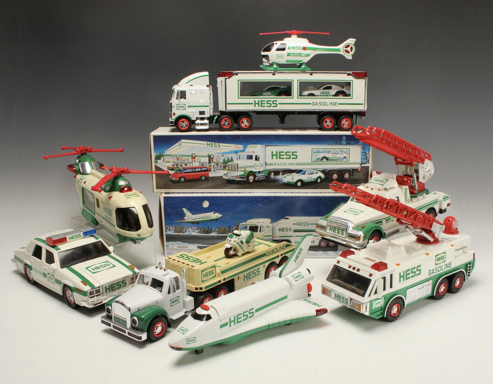 LOT OF HESS TRUCKS & HELICOPTERS: 18 Wheeler 1992 in original box (missing racer), Patrol Car 1993, Rescue Truck 1994, Helicopter 1995, Emergency Truck 1996, Truck and Racers 1997, Truck and Space Shuttle with Satellite 1999 in origin