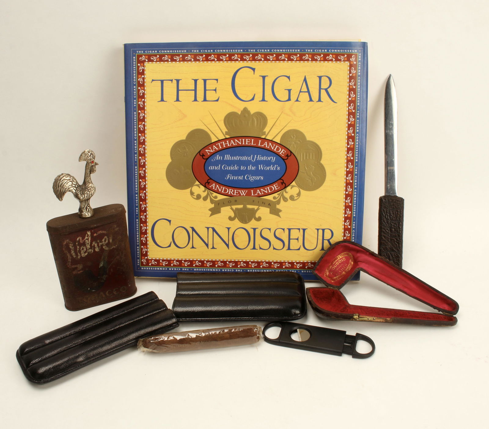 CIGAR CONNOISSEUR BOOK AND ACCOUTERMENTS: Coffee table book on cigars, leather cigar case, snips, and 1 Judges Cave cigar, Pipe case stamped A. Dubois Paris, letter opener, vintage Velvet pipe tobacco tin, and metal rooster made in Portugal.