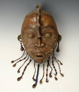 CAST BRONZE TIKAR MASK GABON: Cast Bronze Tikar Mask GabonBronze mask with heart shaped mouth area, diagonal and sun patterns on cheeks, joined brows, nail head embellishments on the hair. Conch shell and trade bead pendants