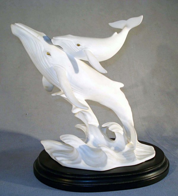 Whales by Lenox: A white and gold bisque porcelain or bone china of a whale and its calf amidst a watery environment. The bottom marked "Song of the Whale", and Lenox, 1992. Set onto an ebonized wood stand, about 7 1/