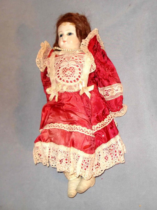 Doll in red and lace dress : A 12" doll with a satin like and lace dress and string of pearls and biscuit head, ceramic arms and leather jointed body.