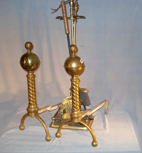 Andirons and fireplace utensils: A pair of hollow brass and cast iron andirons, 21" x 10" x 17", together with a brass fireplace set consisting of a shovel, iron log support, and brush all with a brass storage rack.