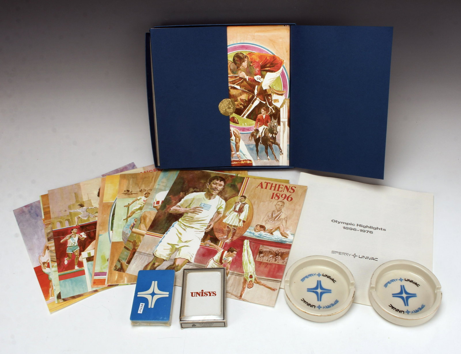 SPERRY UNIVAC COLLECTIBLE LOT PLAYING CARDS BOOK: SPERRY UNIVAC COLLECTIBLE LOT PLAYING CARDS BOOK Sperry Univac Olympic Highlights book with 16 prints spanning the years 1896-1976 in box, two ceramic ashtrays, and two packs of playing